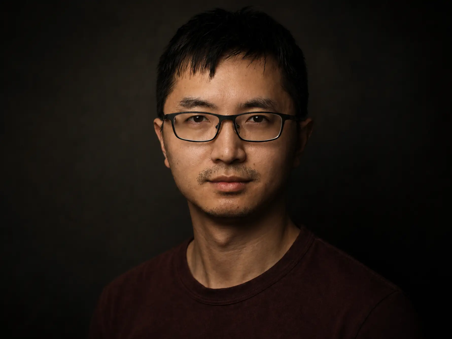 INT21 founder and CEO Bing Xu, wearing a black shirt and black glasses in front of a black background.