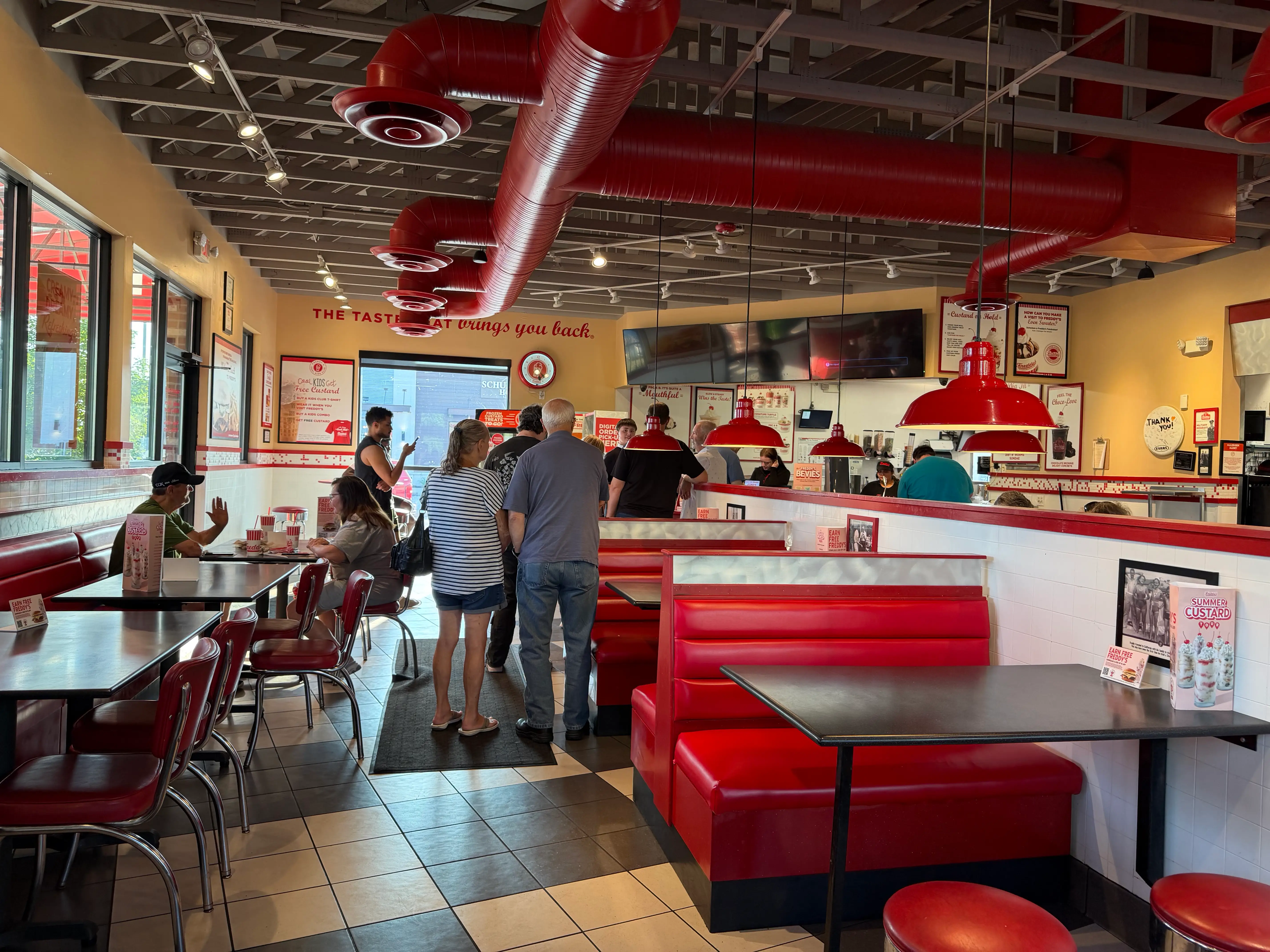 Line inside a Freddy's with view of checkered floor, red leather booths and chairs