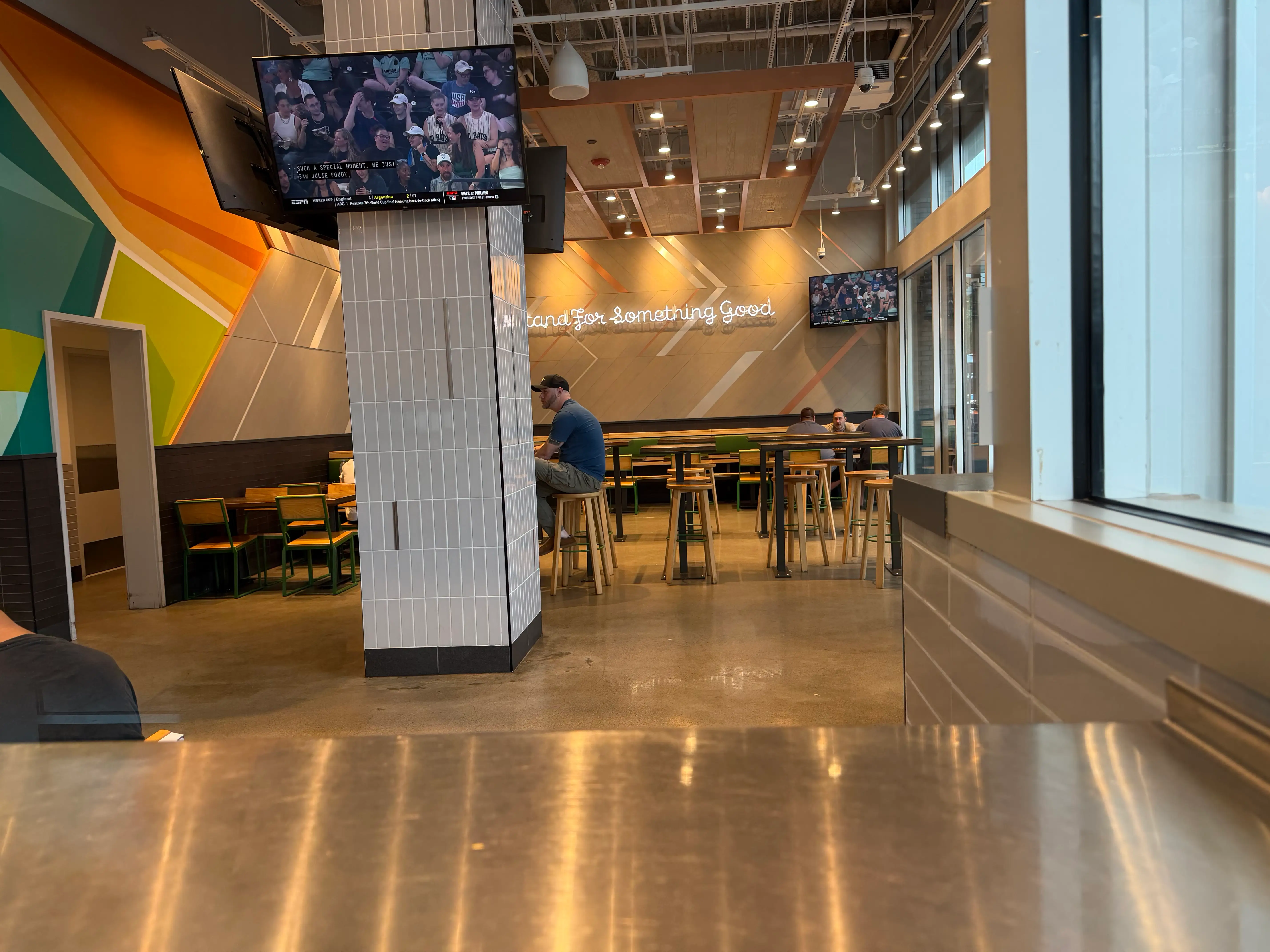Interior of Shake Shack with high-top tables and stools, concrete flooring, colorful wall mural