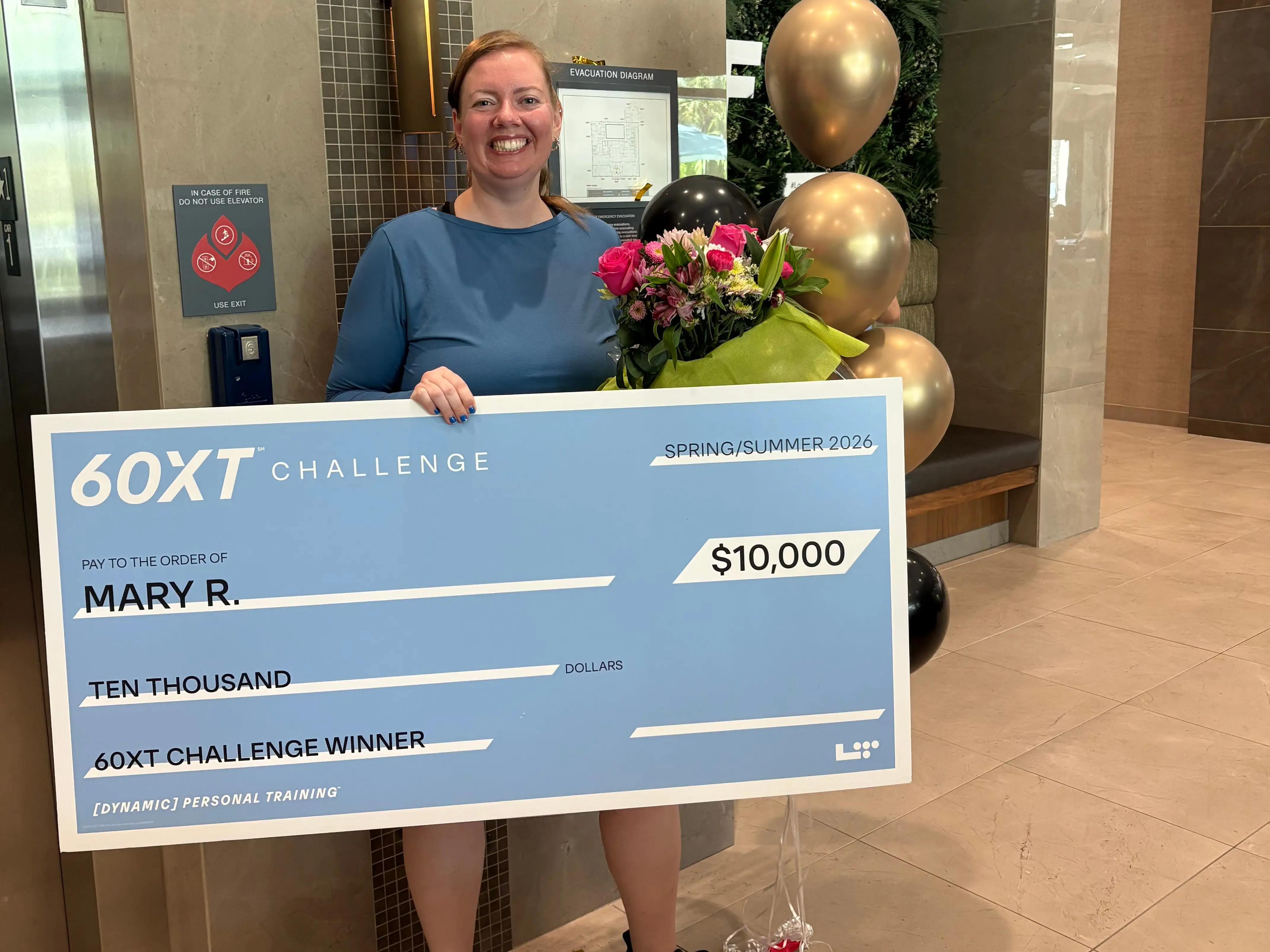 A woman holding a giant check and some flowers.