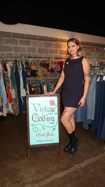 Hannah Valentine, dressed in a dark vintage dress with black boots, is standing next to a sign labeled 