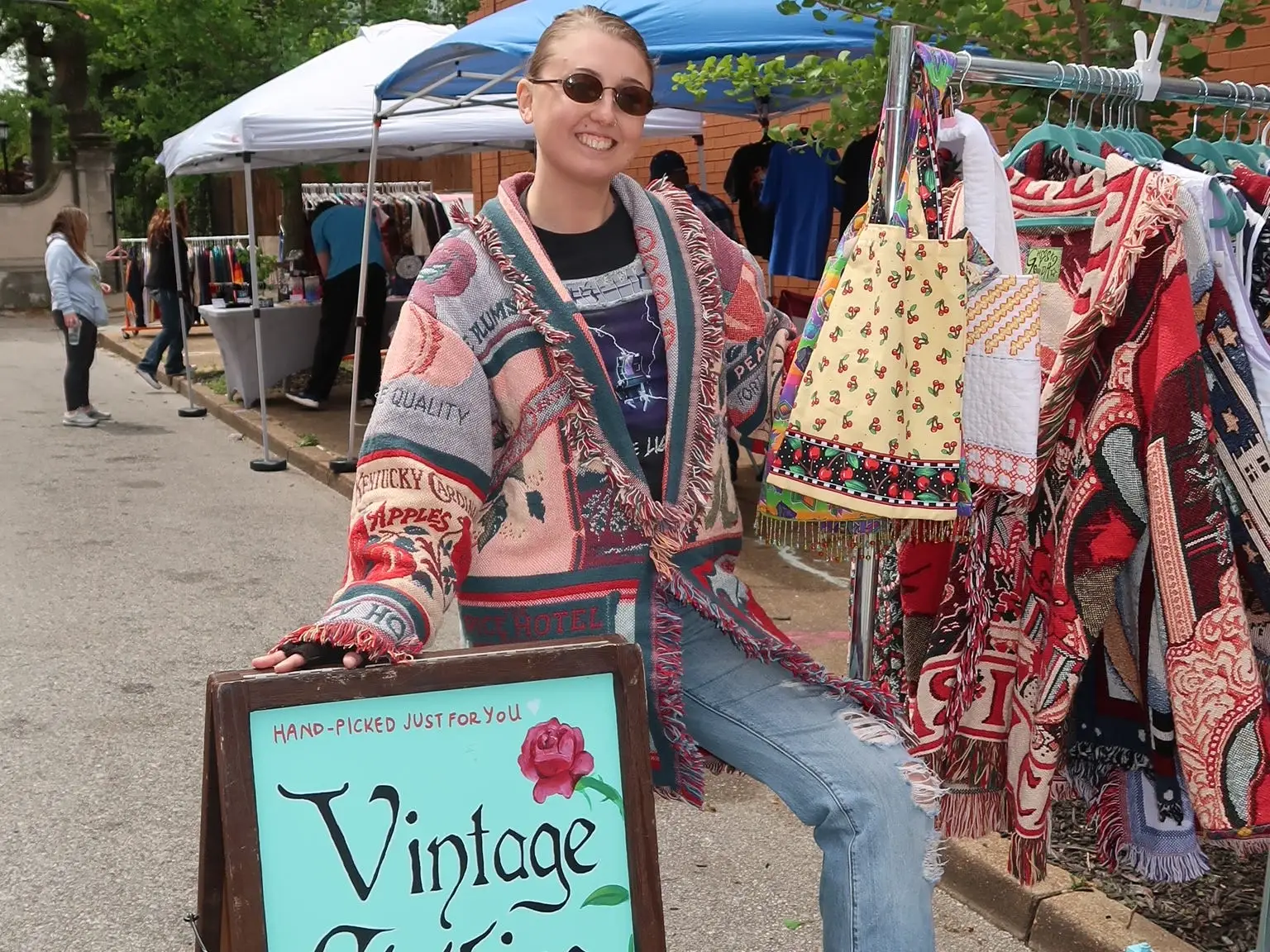 Hannah Valentine is standing outside in a colorful vintage coat and ripped jeans.