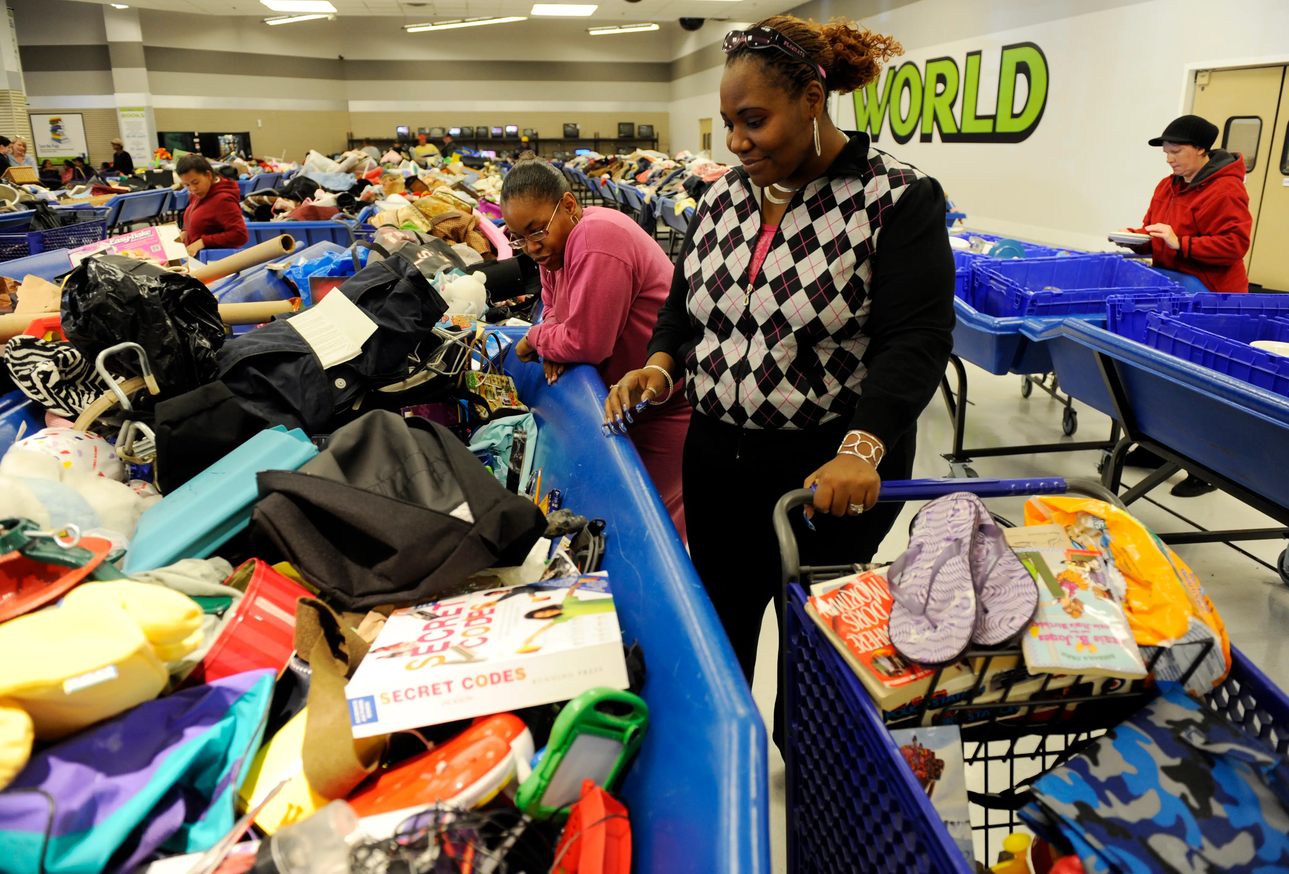 Two women search through bins of clothing, toys, and household goods at the Goodwill Outlet World store in Aurora, Colorado.