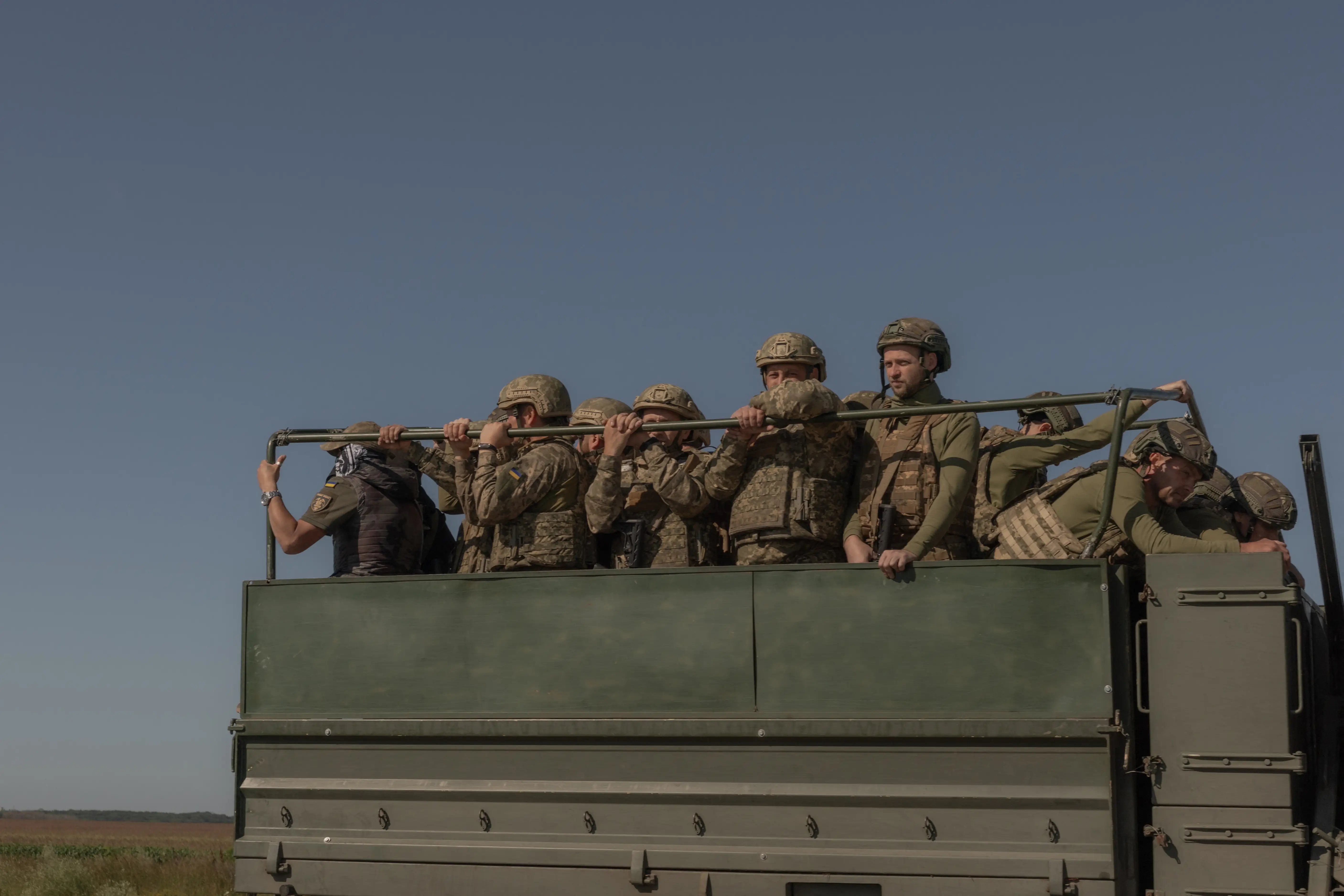 Ukrainian soldiers sit on the back of a truck.