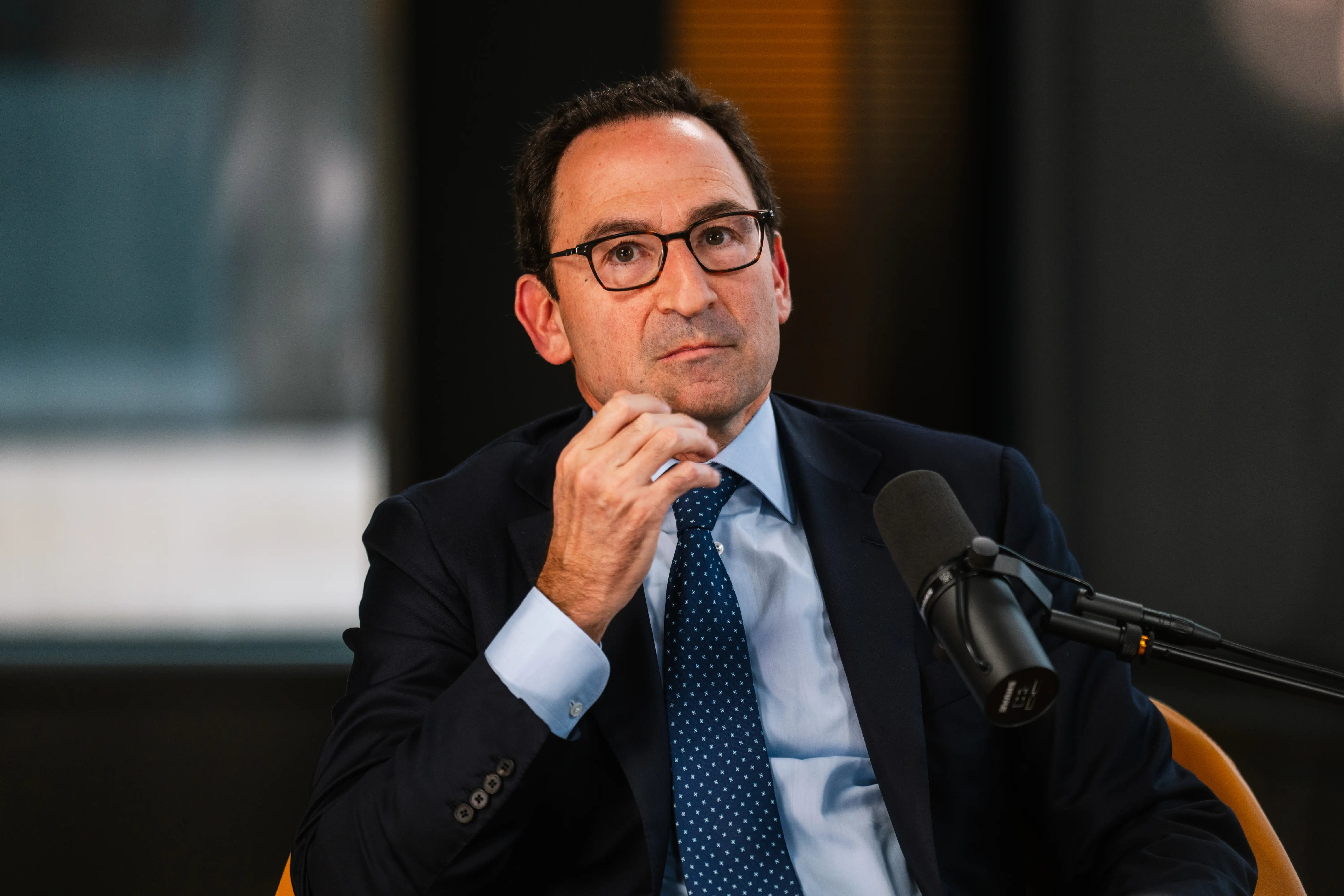 Blackstone President Jonathan Gray in a dark suit and glasses sits beside a studio microphone during an interview