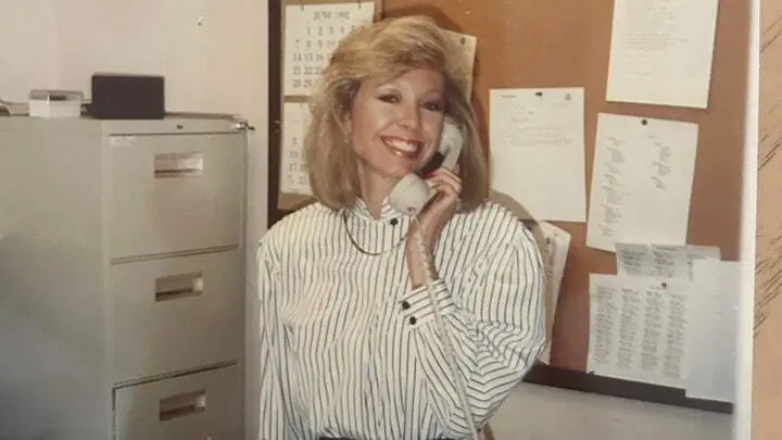 Old photo of a young Jana Monroe on the phone in an office setting.
