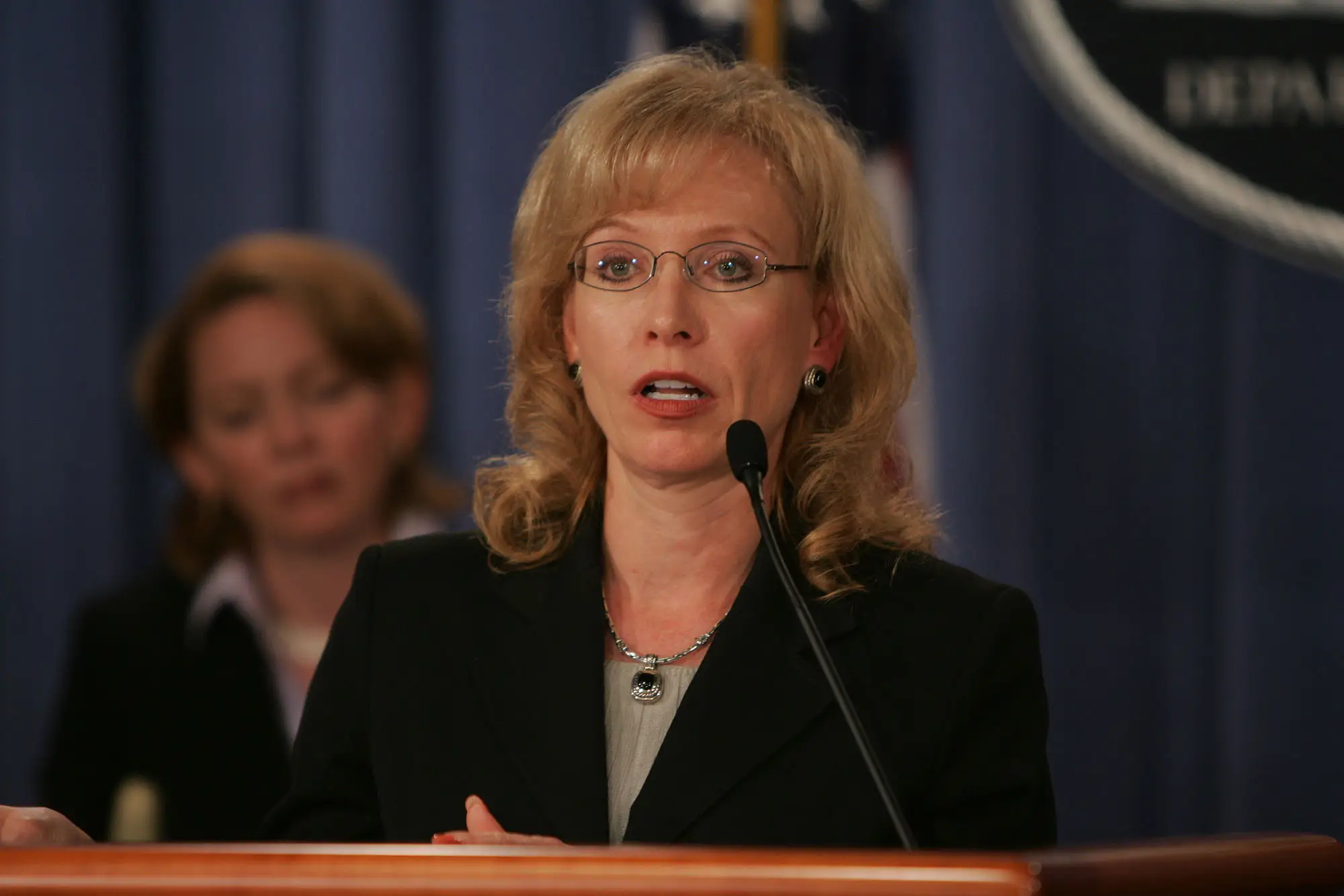 Jana Monroe, dressed in a suit at a podium, at the U.S. Department of Justice in Washington, D.C. in 2004.