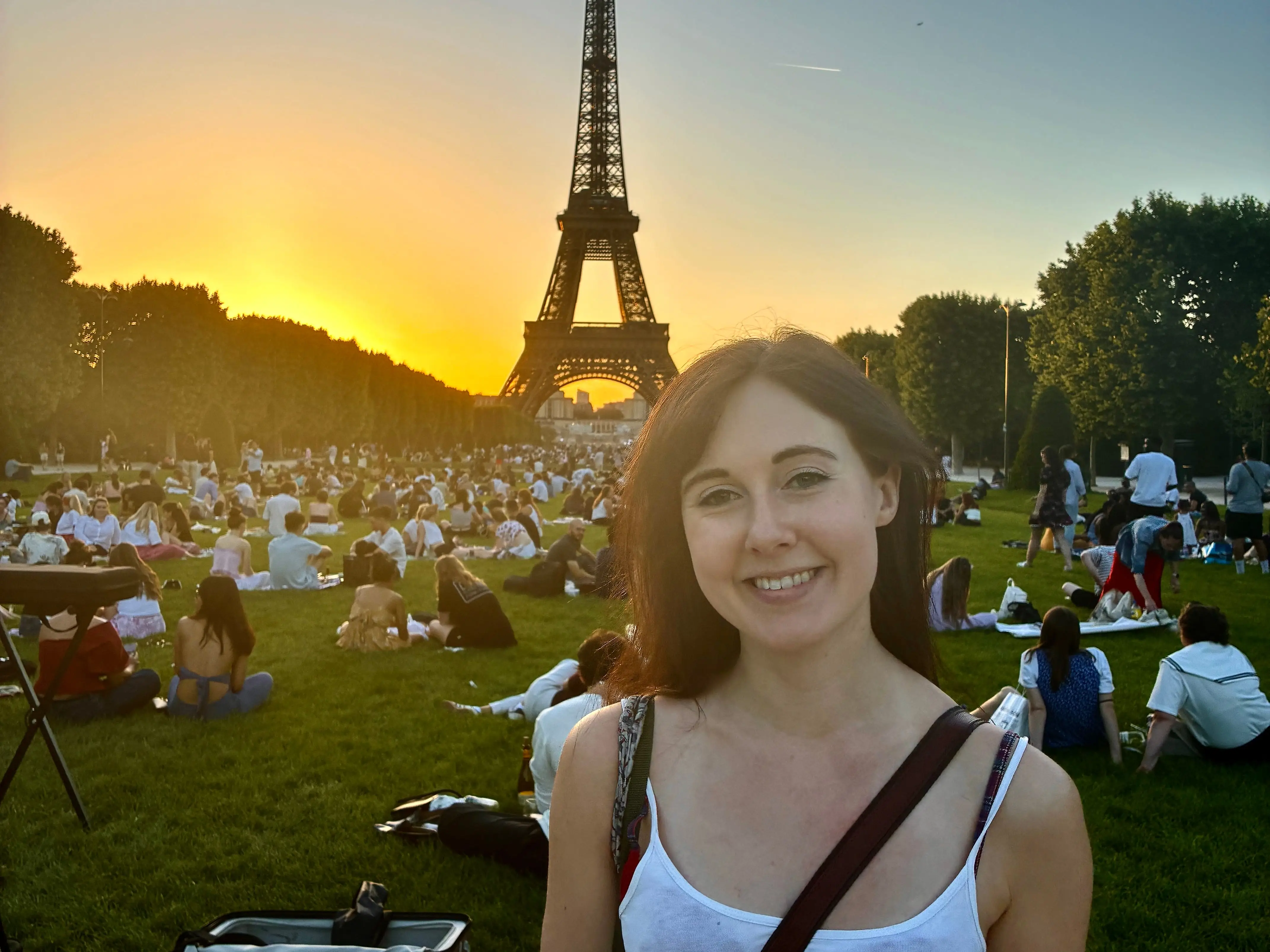 Woman smiling in front of grass with people on it in Champ de Mars. with Eiffel Tower in distance
