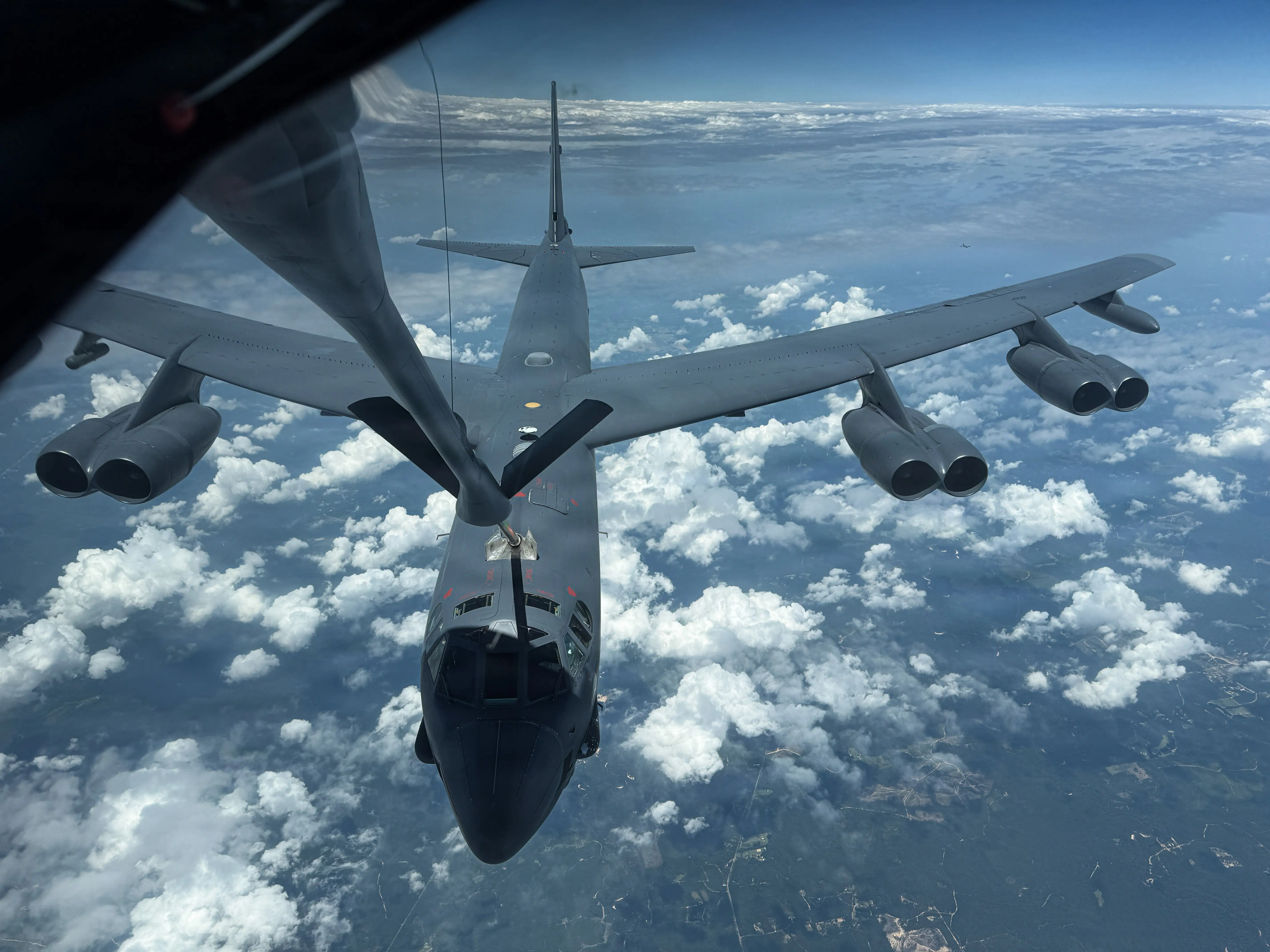 A US Air Force B-52 Stratofortress bomber flies above a landscape.