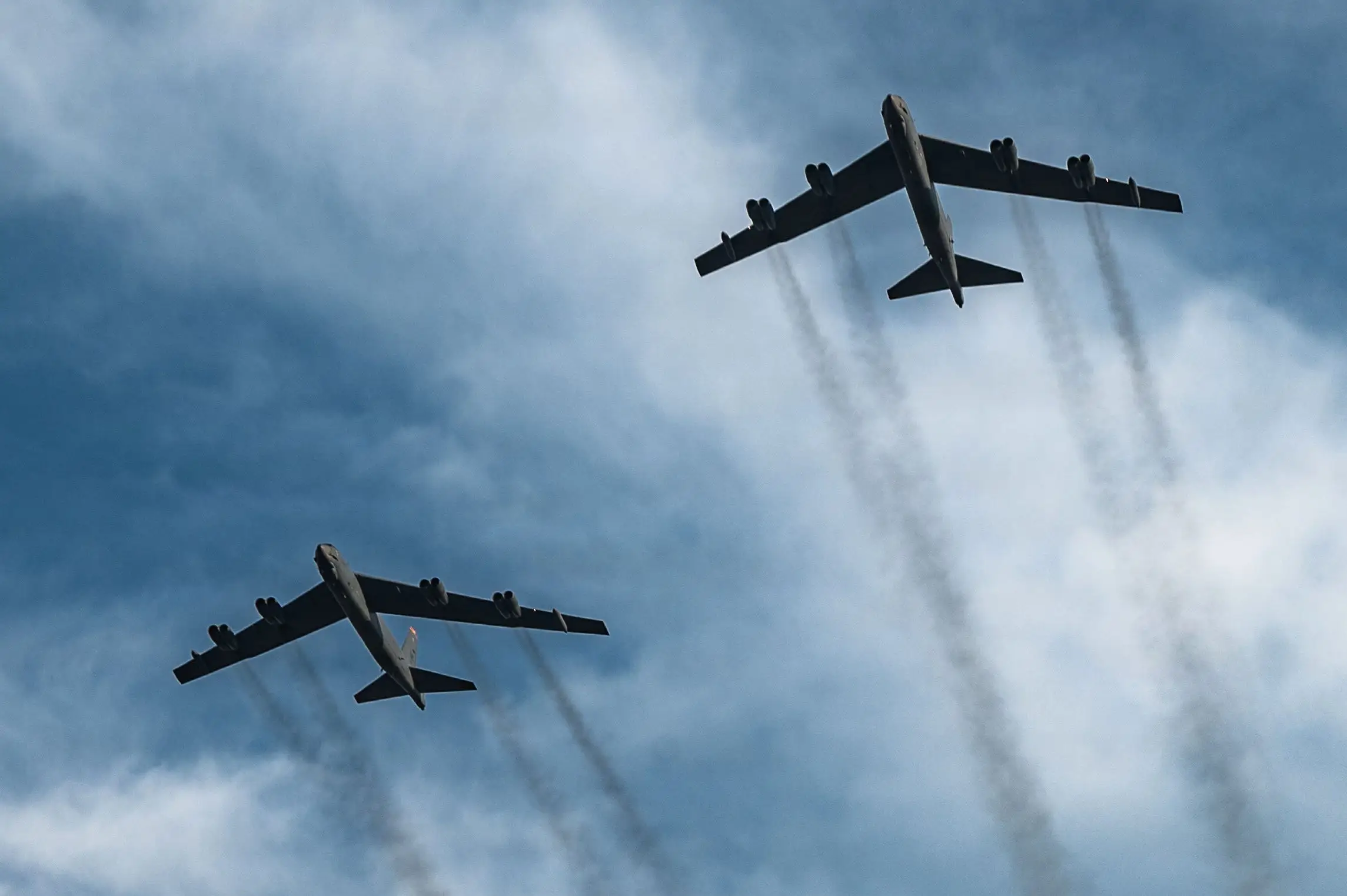 US Air Force B-52 bombers fly over an overcast sky.
