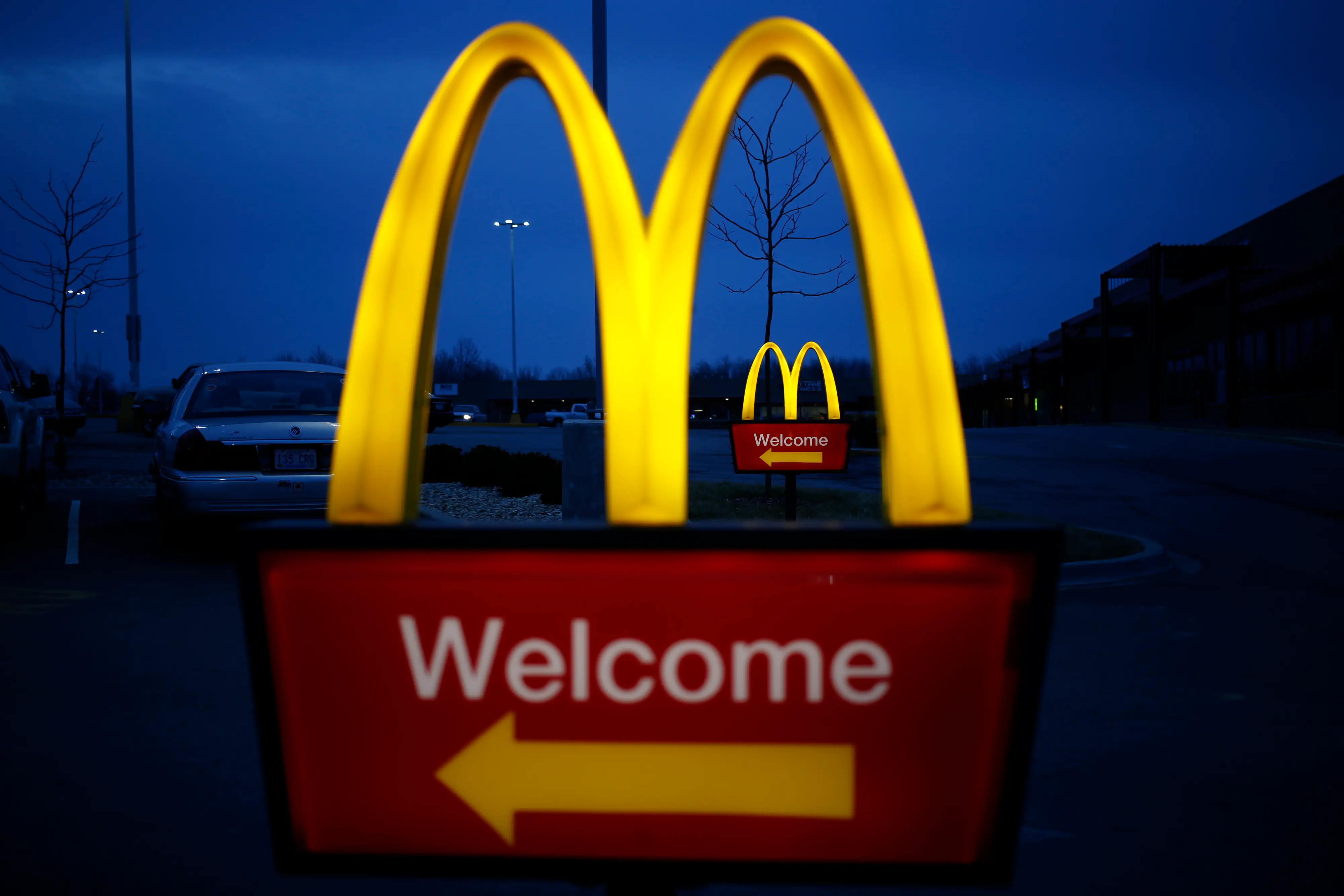 A lighted McDonald's sign points to the drive-thru lane outside a restaurant.