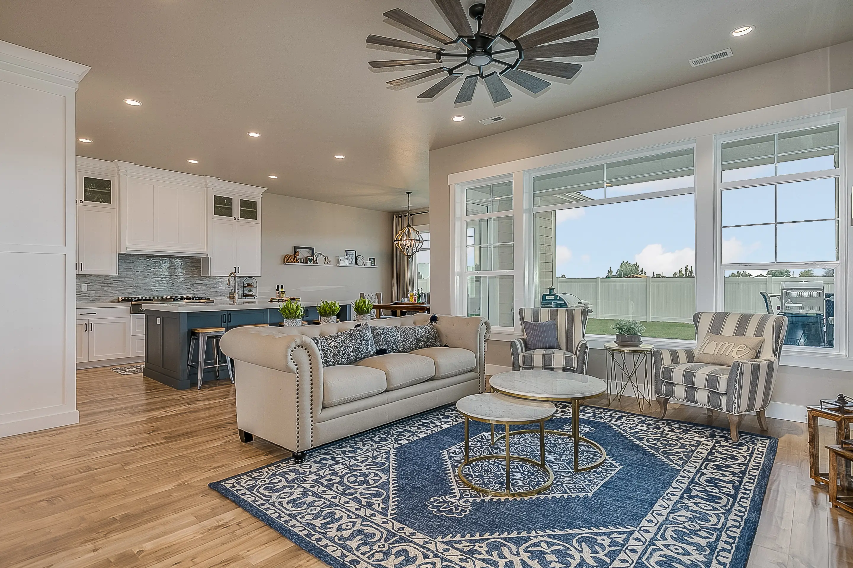 Open concept kitchen and living room with large ceilingfan, blue area rug, beige couch, accent chairs