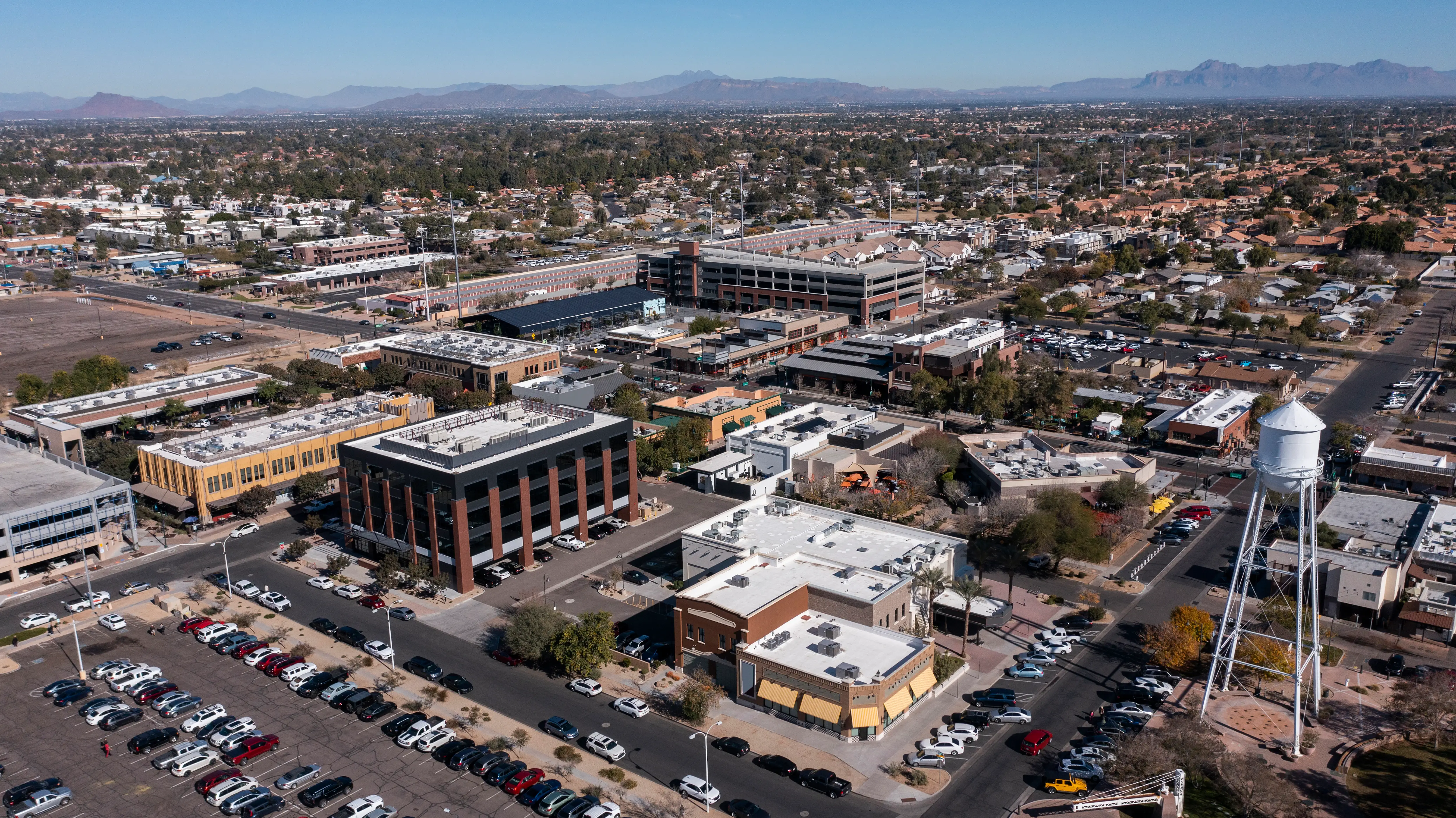 Aerial view of office buildings, parking lots, a water tower, and surrounding neighborhoods with mountains in the distance.