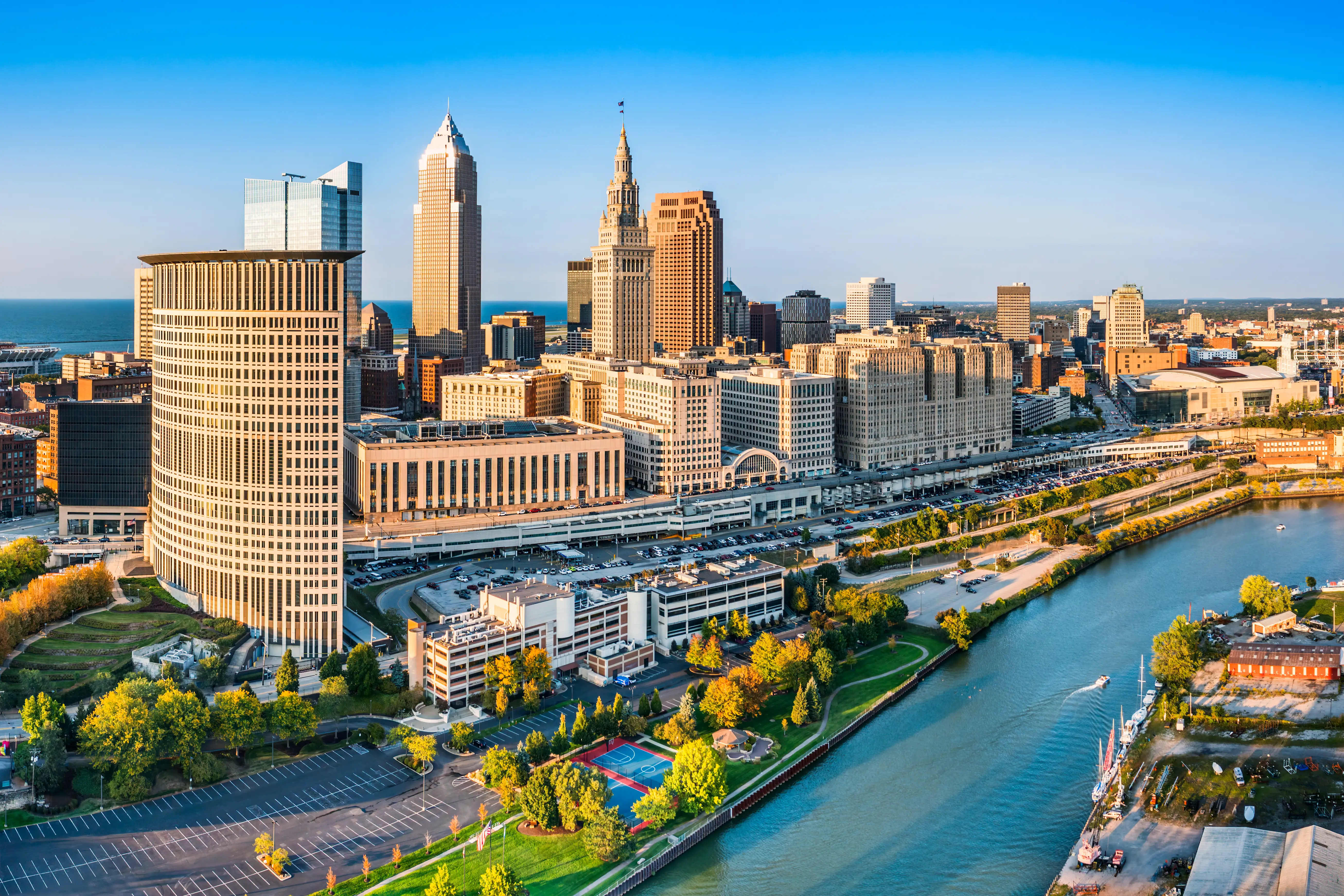 Downtown Cleveland skyline rises beside the Cuyahoga River with Terminal Tower and waterfront parks in warm light.