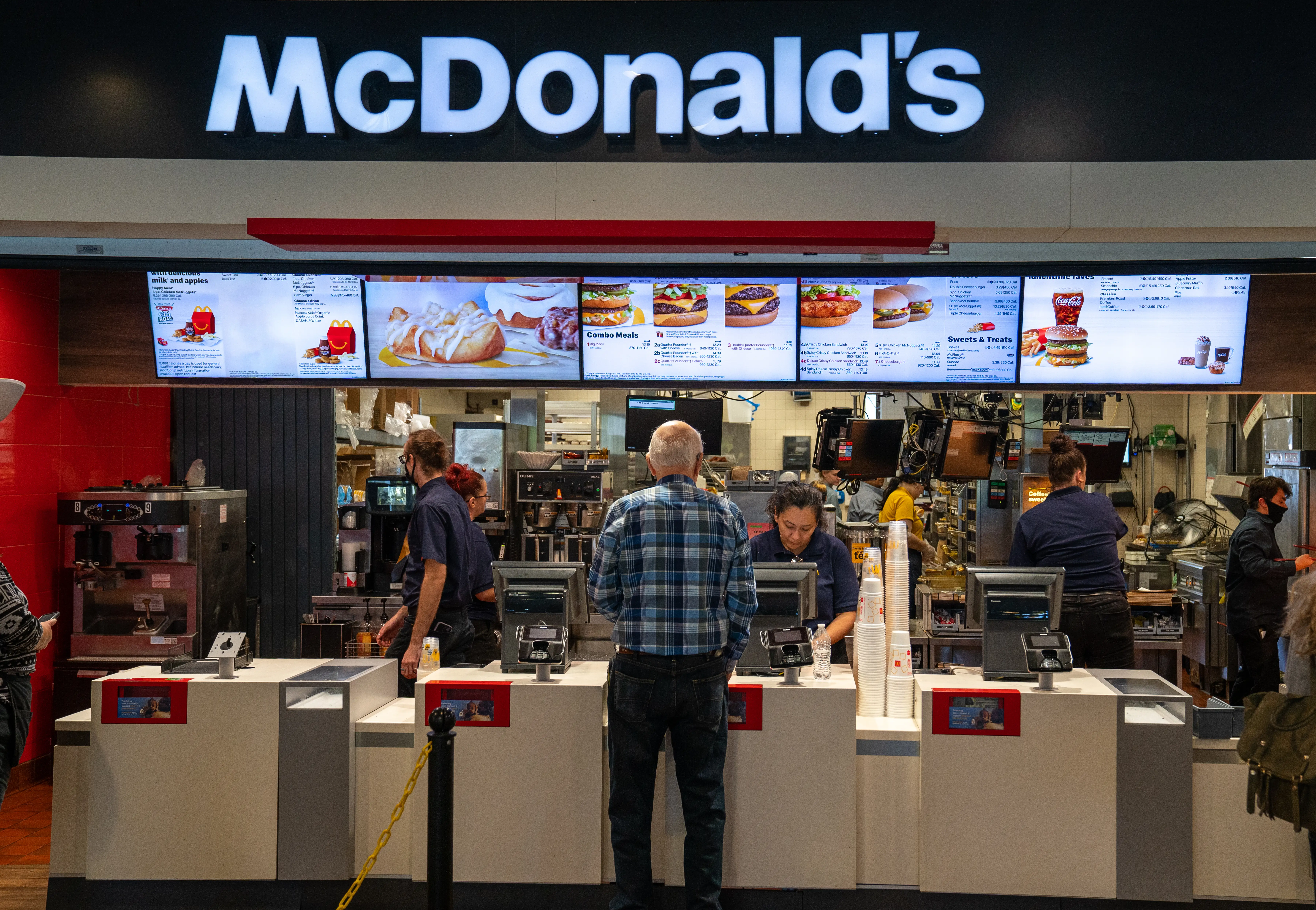 A man orders at the counter in a McDonald's restaurant as workers prepare food and take orders behind the counter.