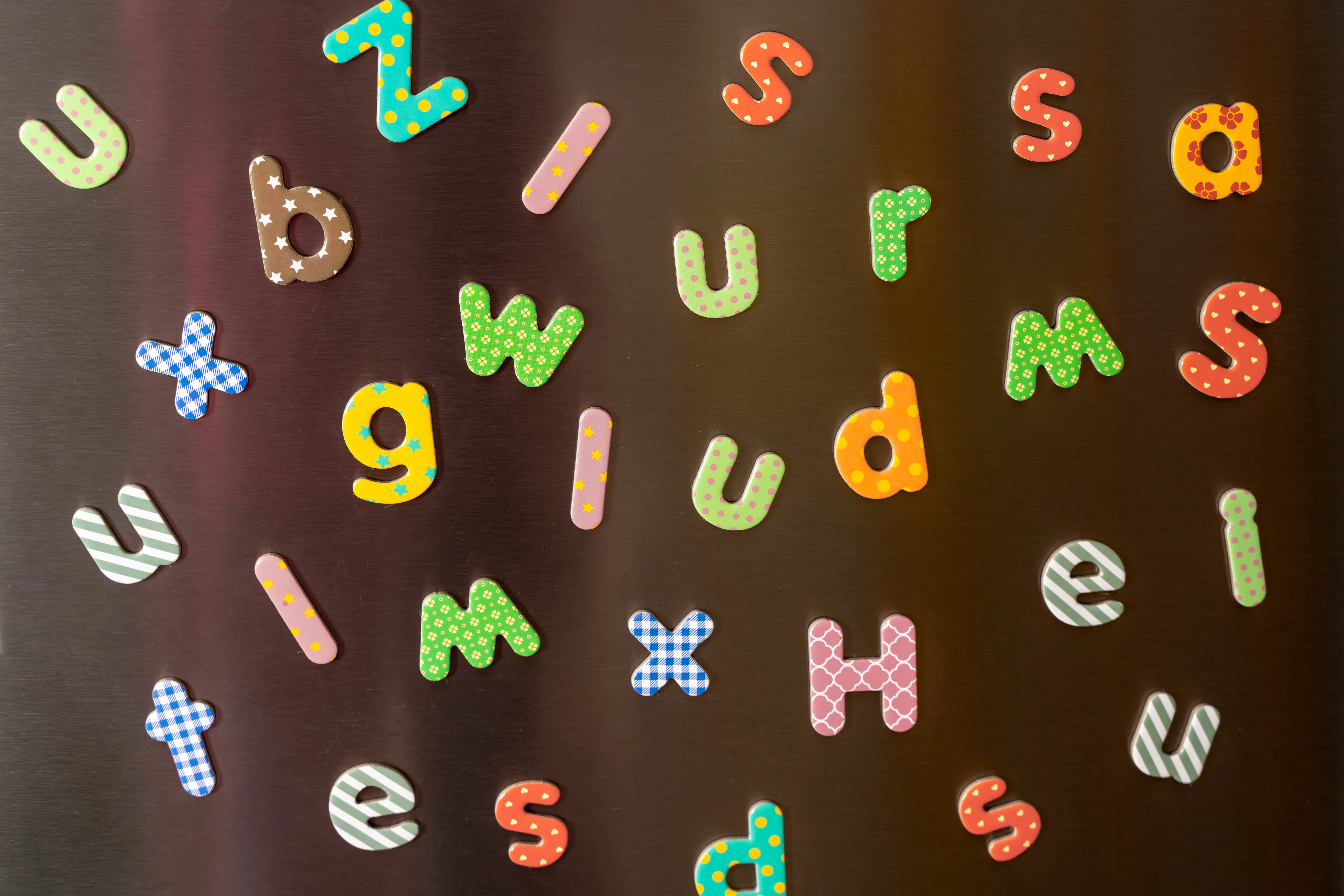 Colorful patterned magnetic alphabet letters are scattered across a dark glossy surface.