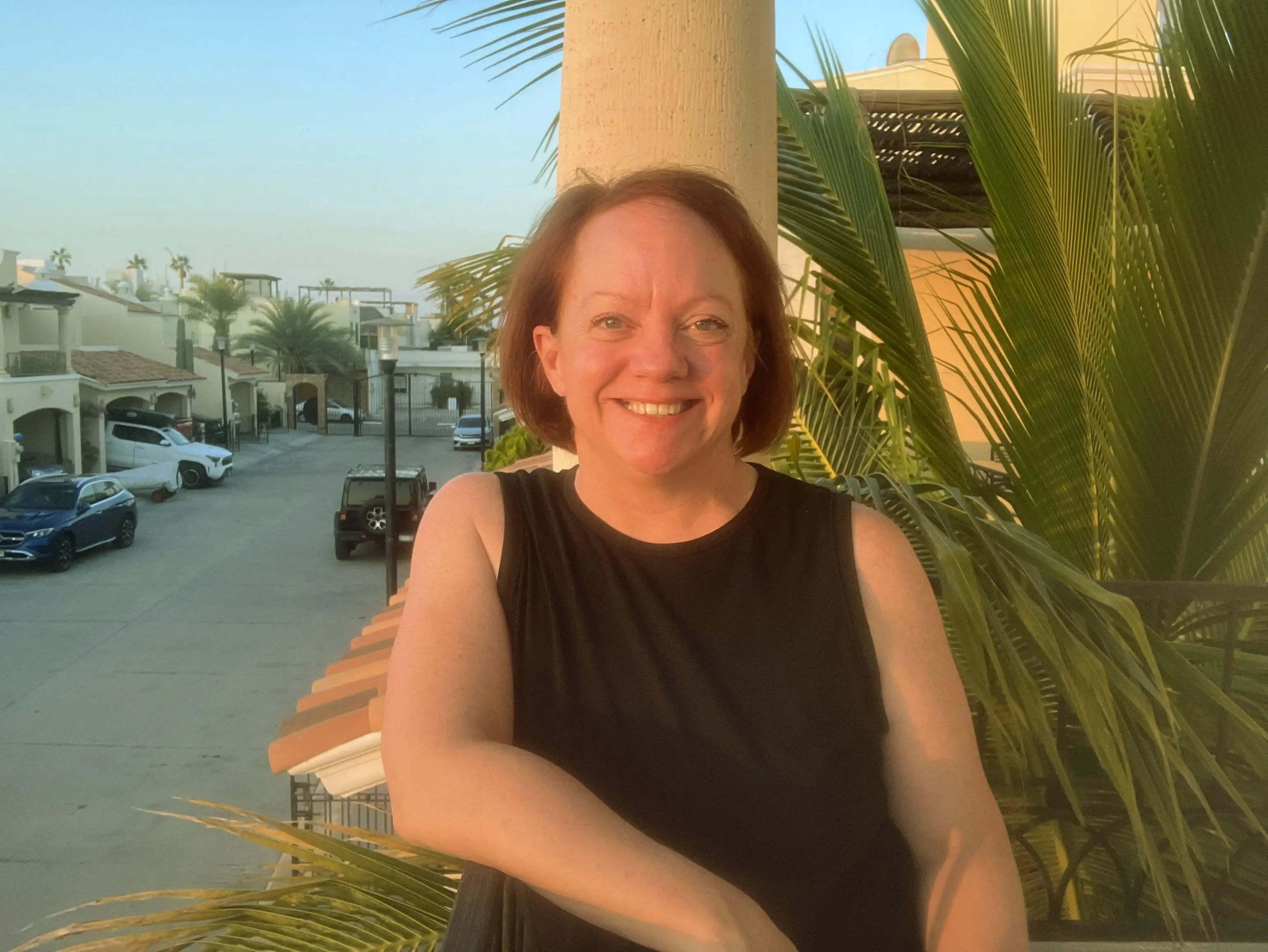 Woman smiling with arm on railing, palm leaves in background in Mexico