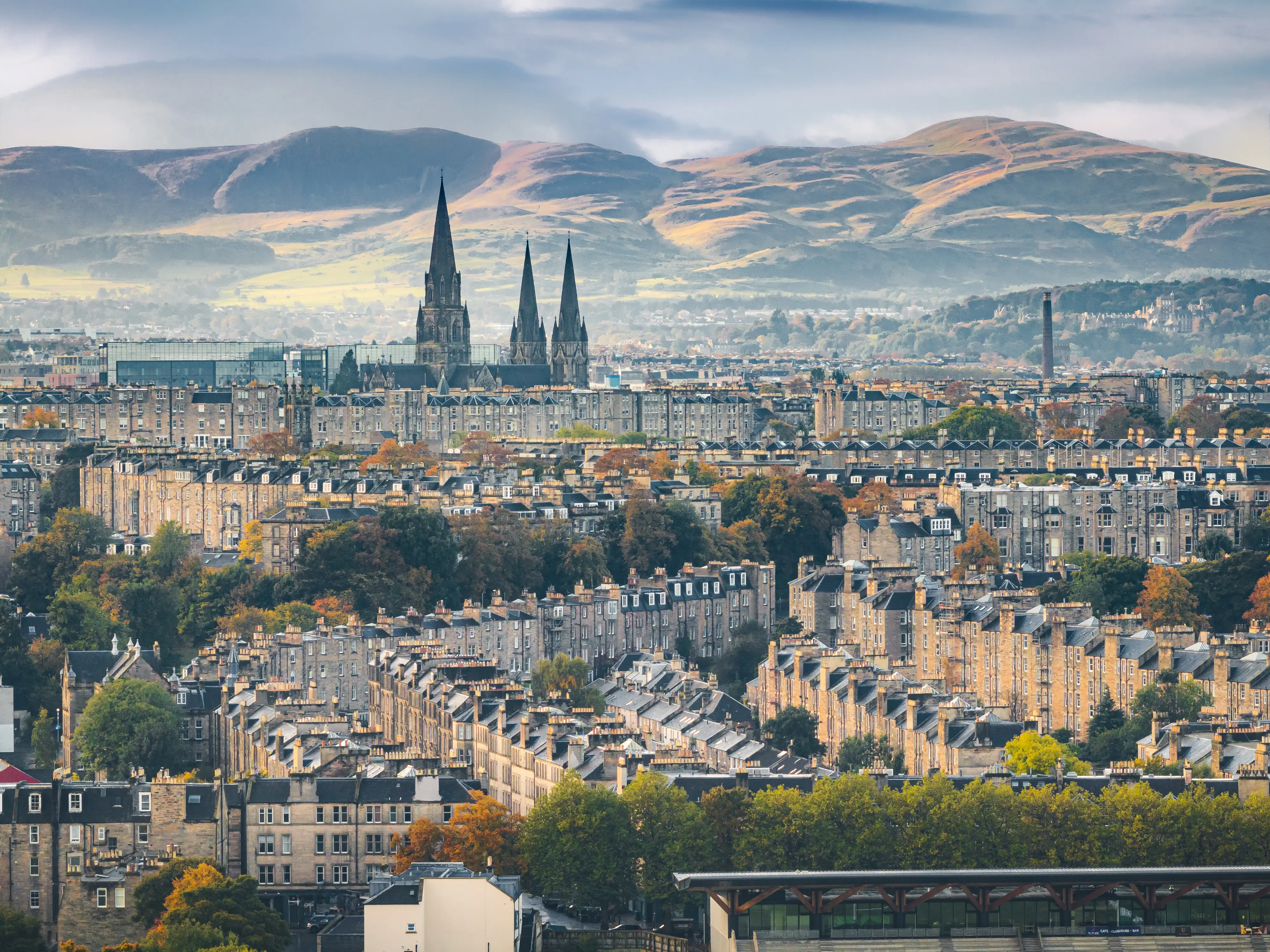 Edinburgh cityscape with St Mary's Cathedral spires rising above stone buildings and hills in the background.