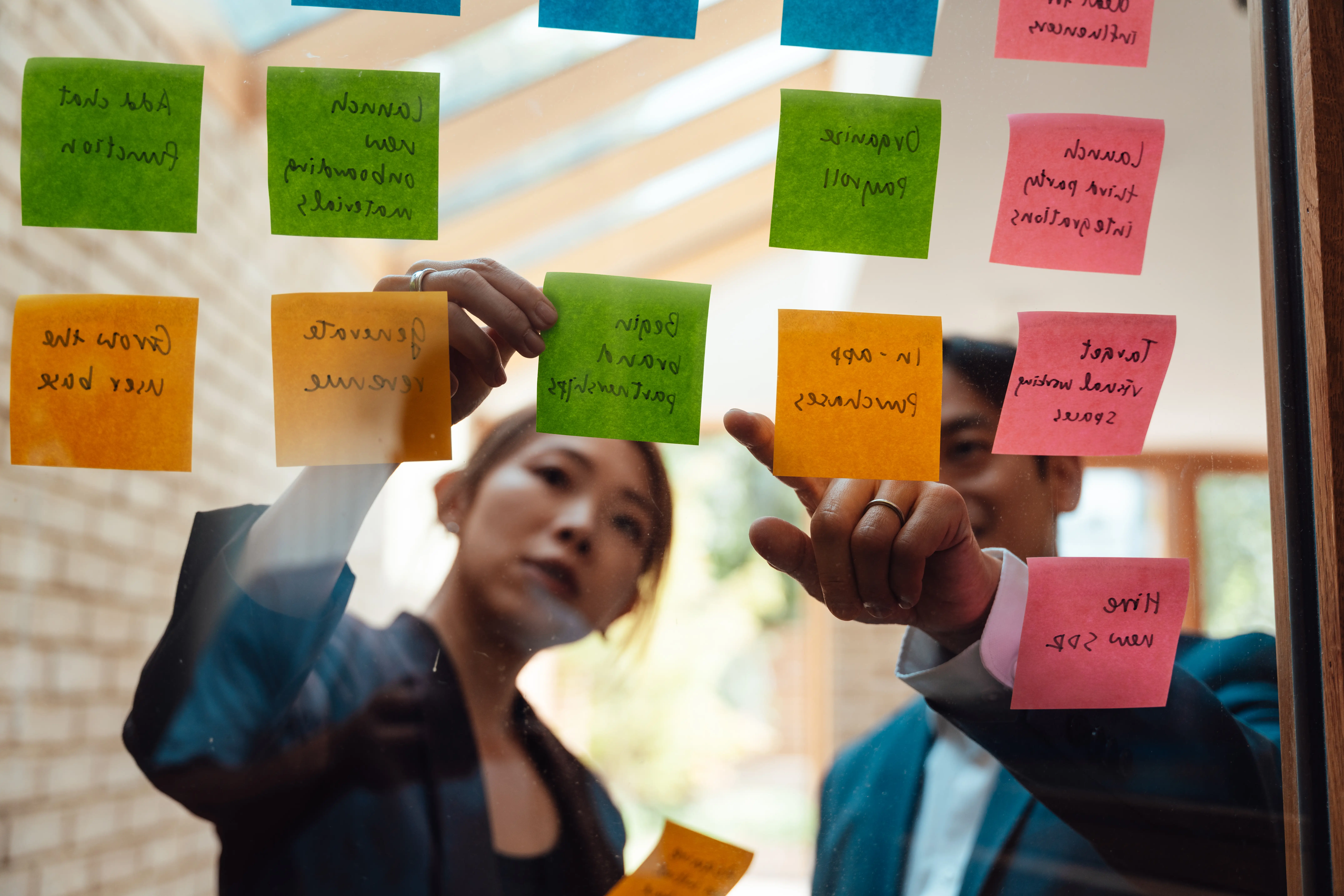 Asian businessman and businesswoman discussing over colourful sticky notes a modern office. Communication and trust in collaboration and teamwork. Business planning and strategy.