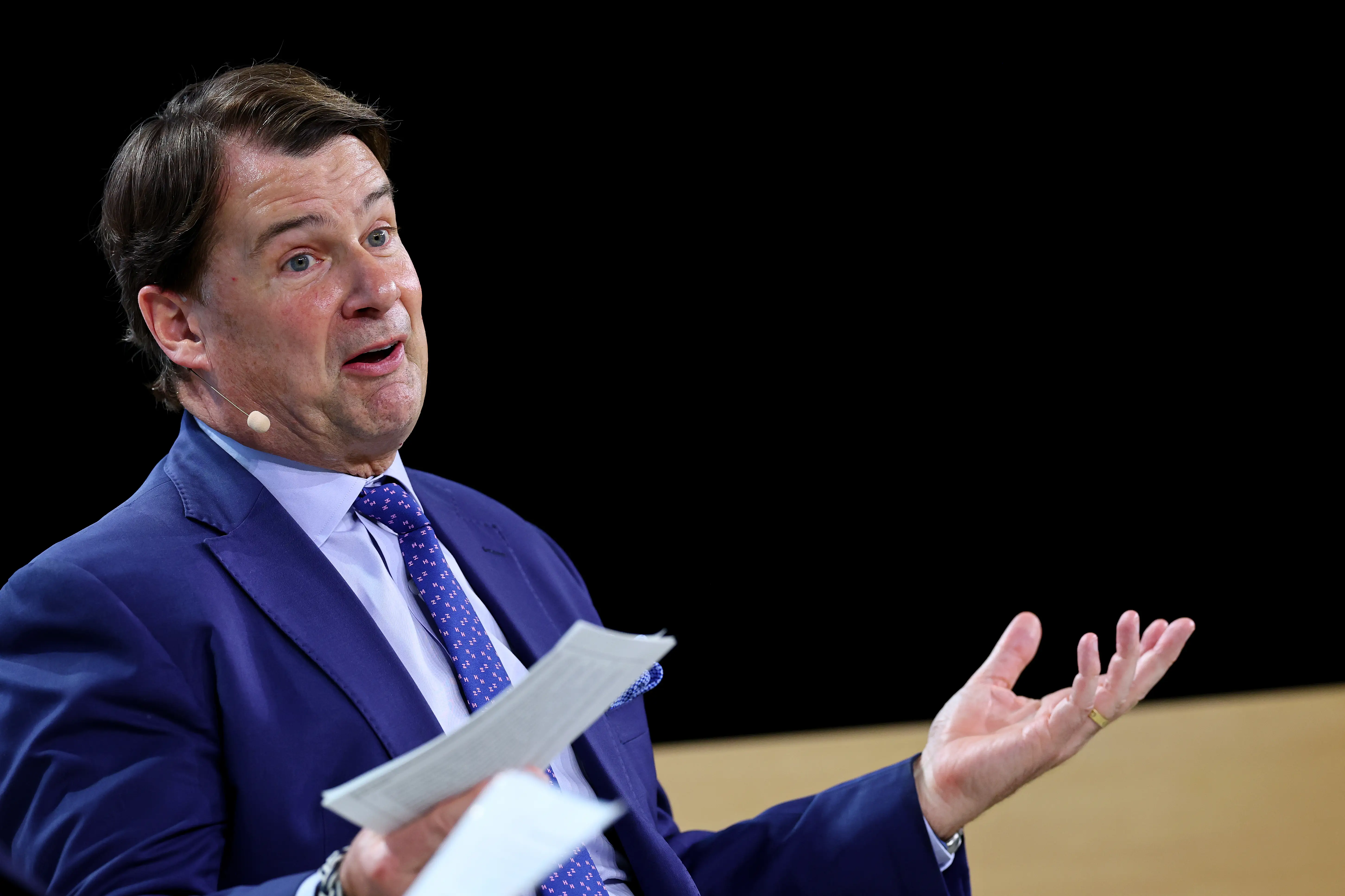 Ford CEO Jim Farley shrugs his shoulders while speaking with cue cards.