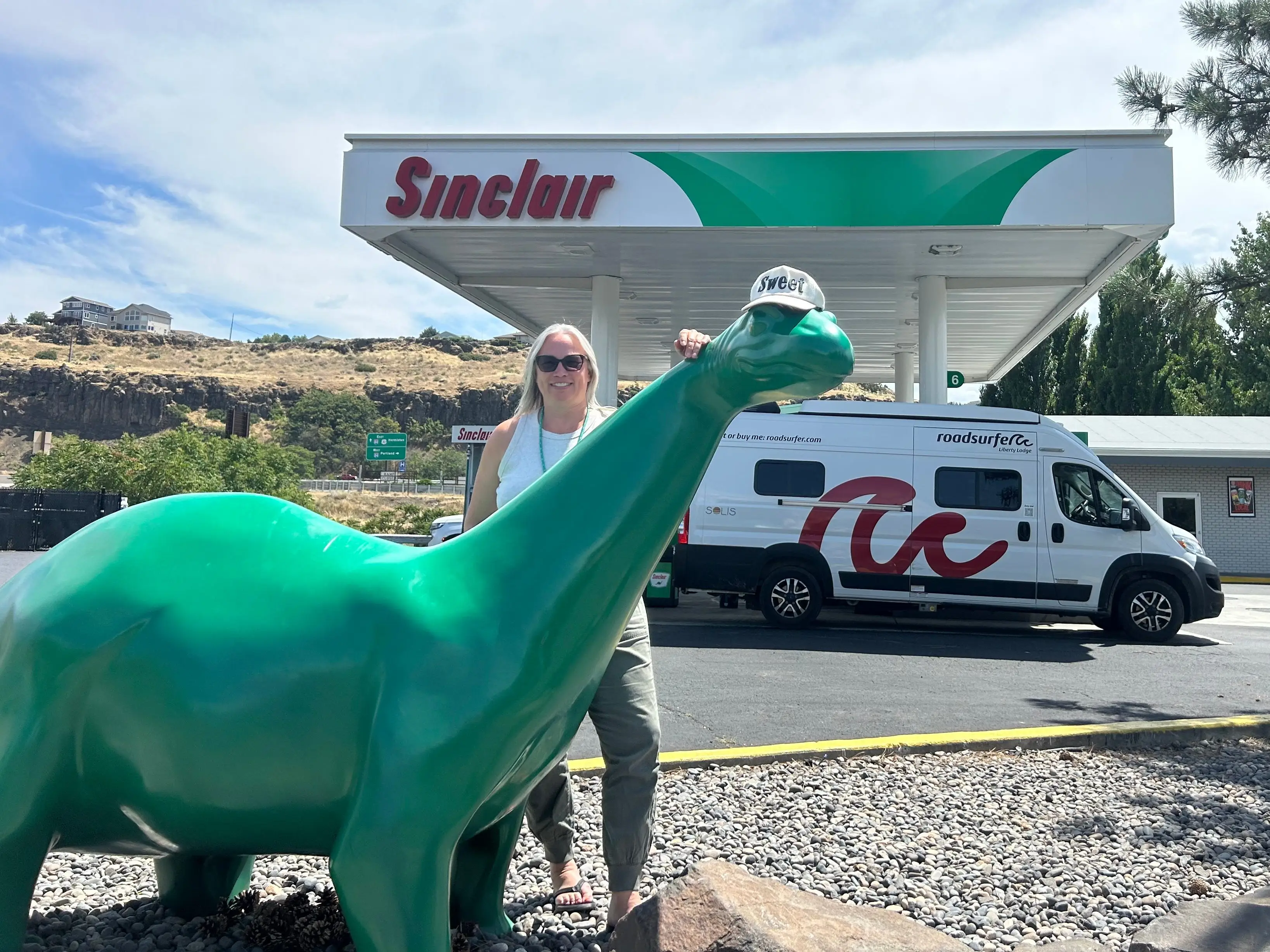 The writer's mother posing next to a plastic dinosaur statue at a Sinclair gas station.