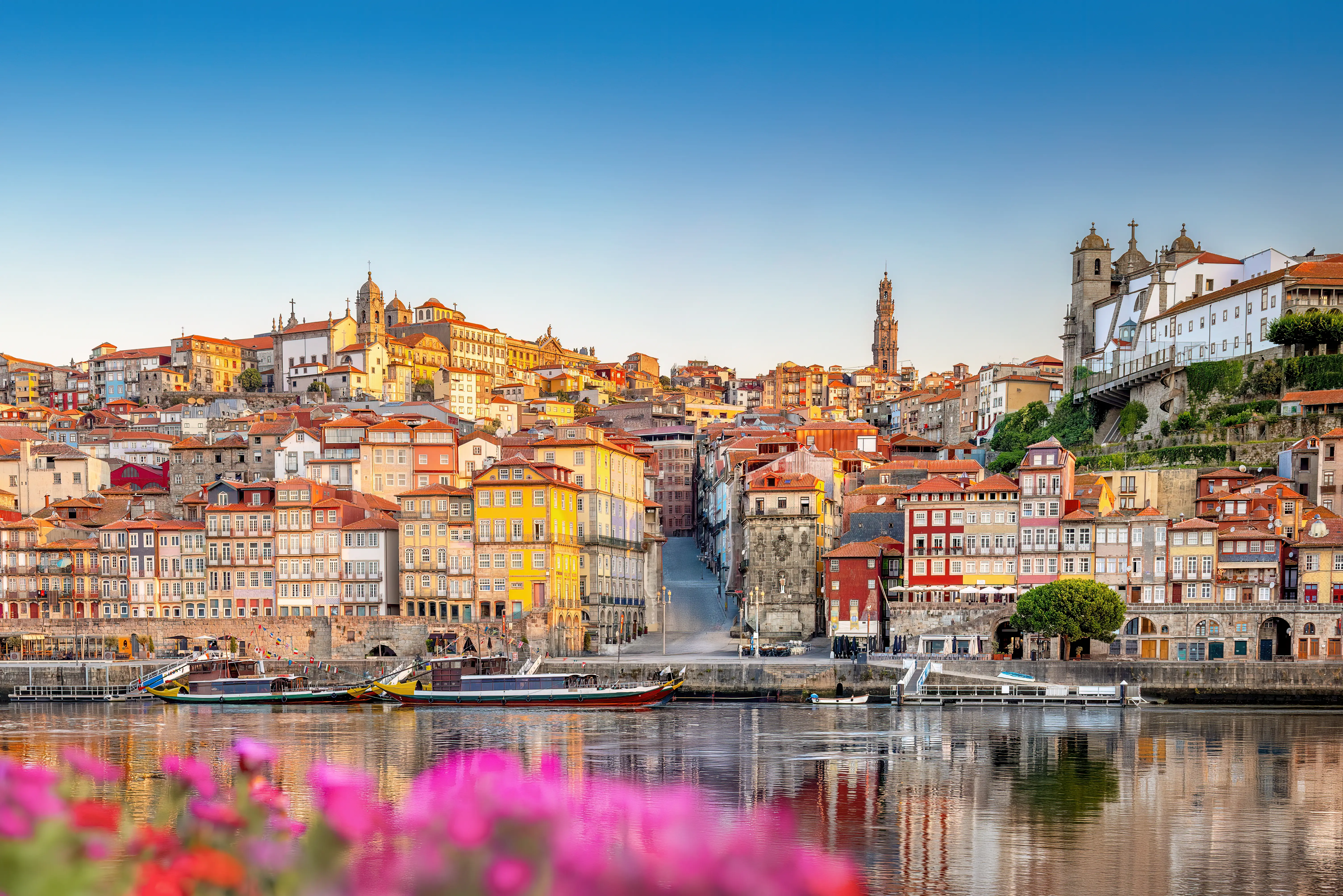 Colorful Porto waterfront buildings and boats line the Douro River under a clear blue sky.