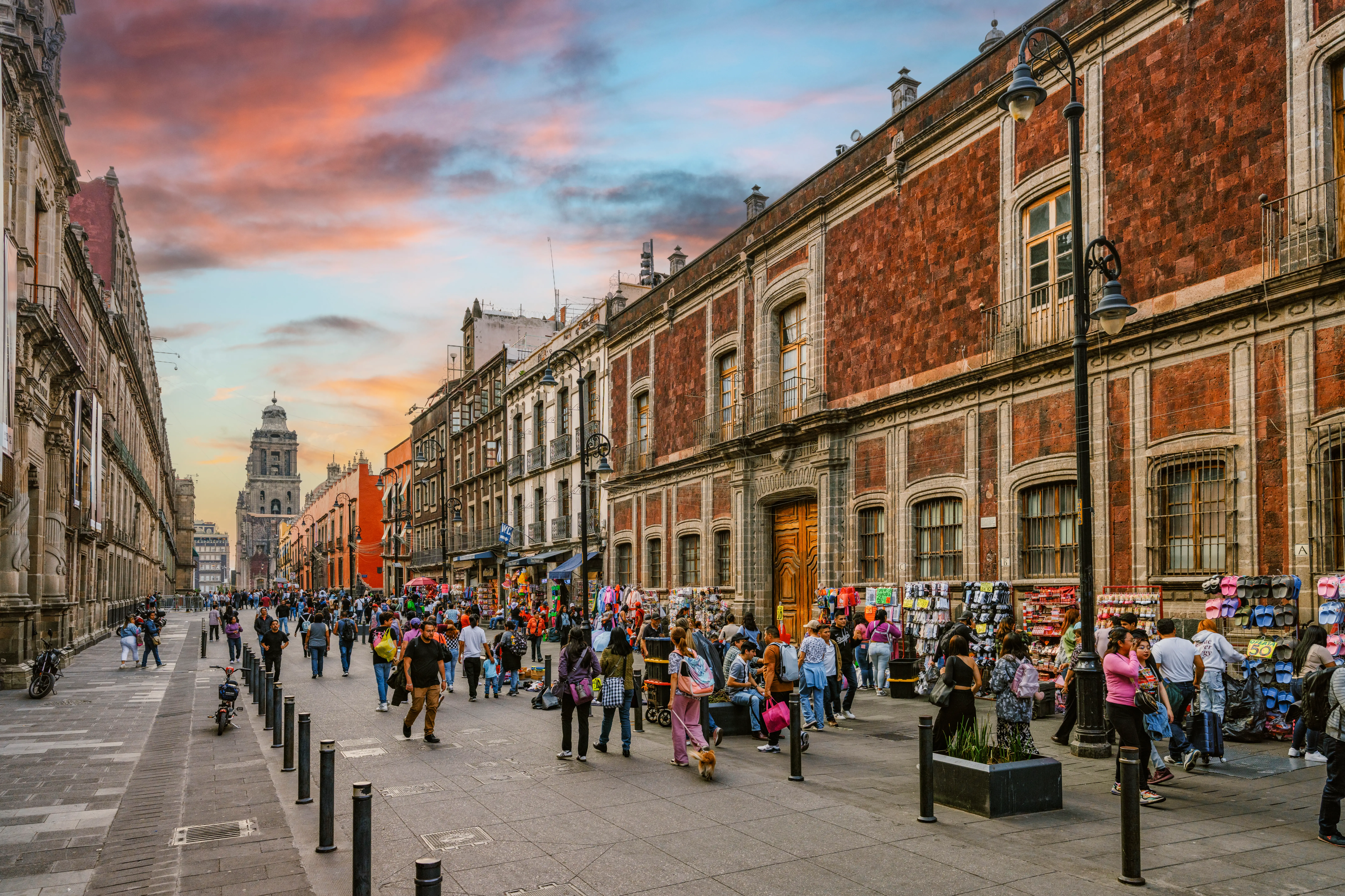 Crowds and street vendors fill a historic pedestrian street lined with colonial buildings at sunset.