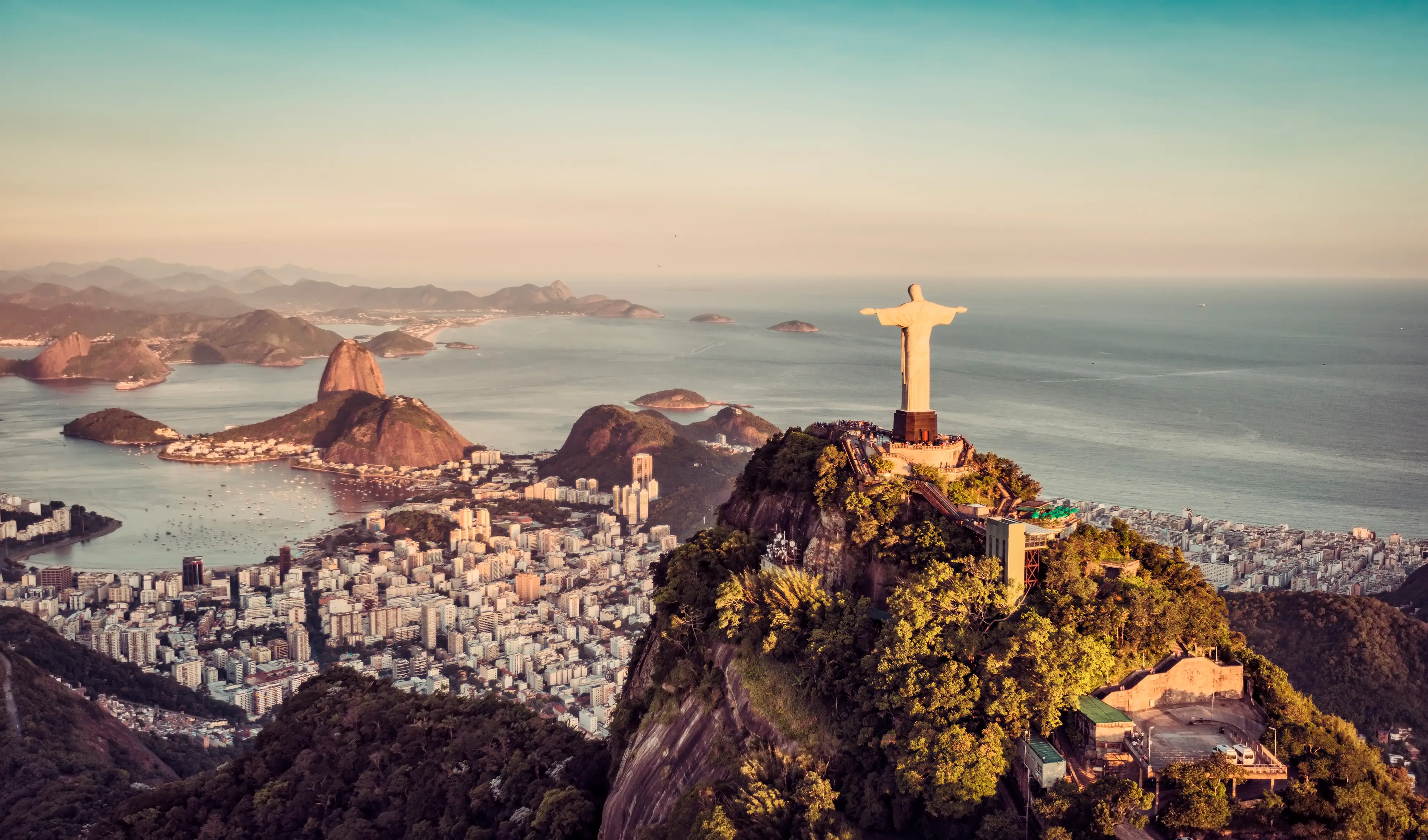 Christ the Redeemer overlooks Rio de Janeiro’s coastline, mountains, city neighborhoods, and Guanabara Bay at sunset.