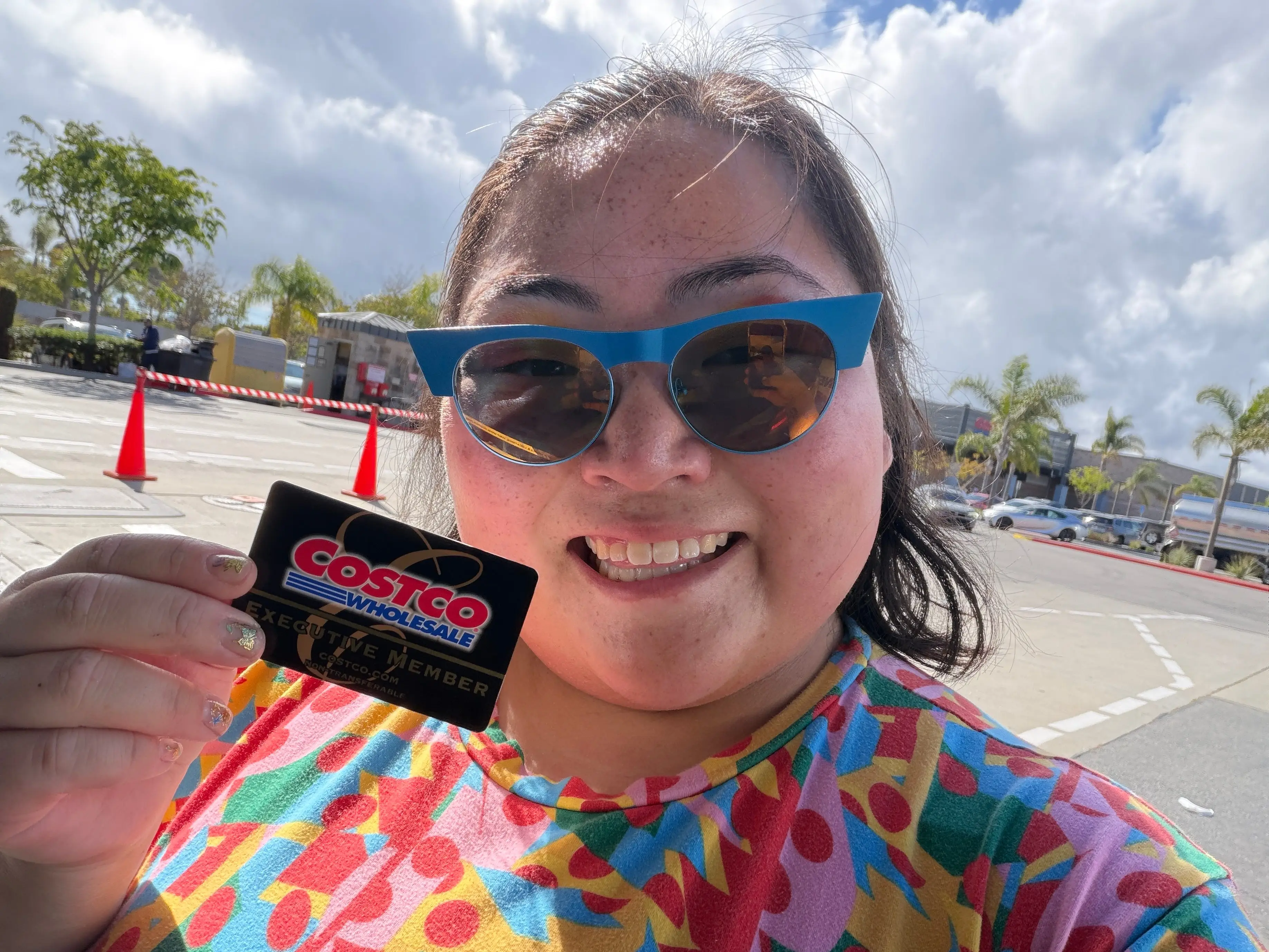 The writer wearing a colorful, patterned top and holding a black Costco card.