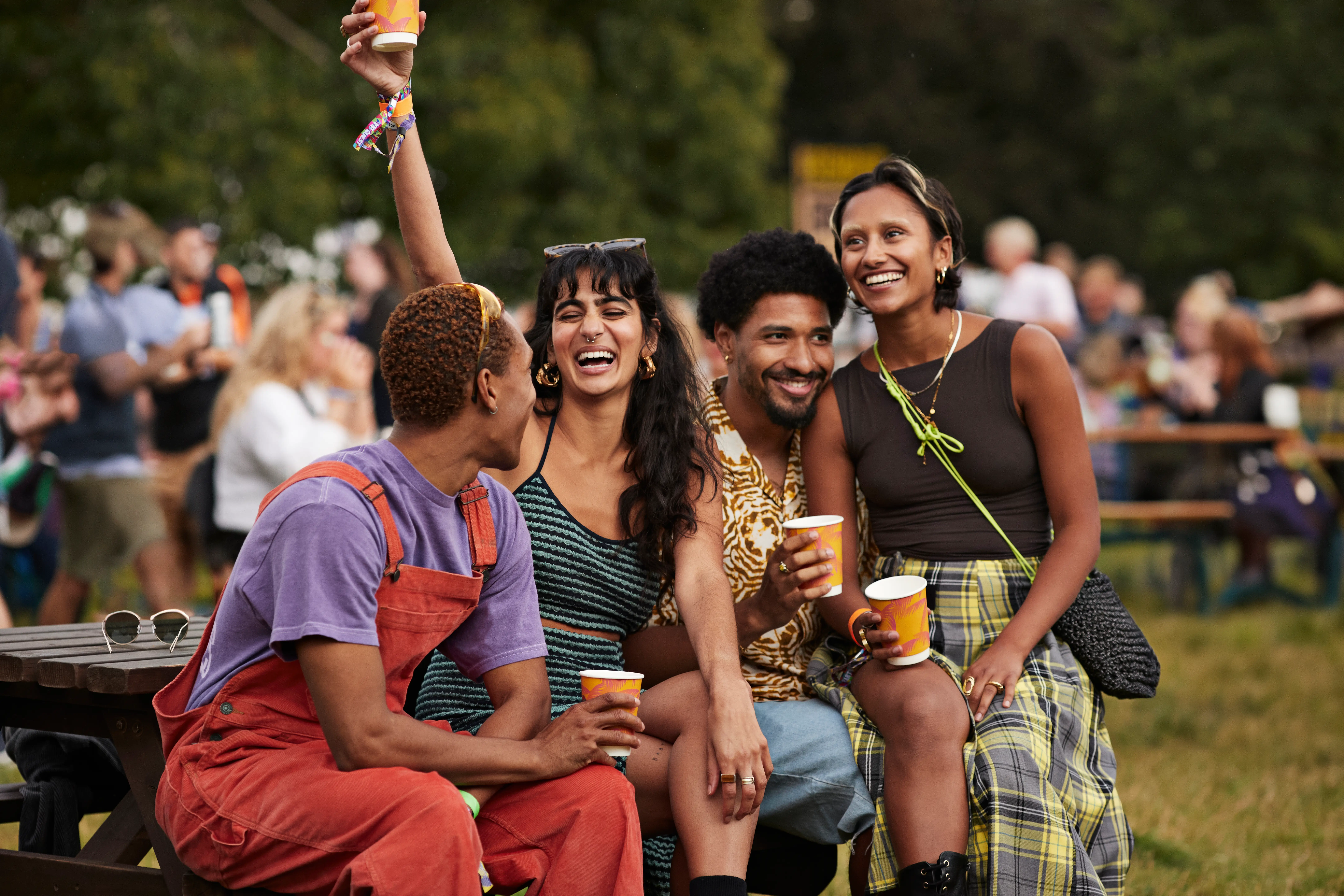 Happy couples sitting with drinks in disposable cups at a music festival.