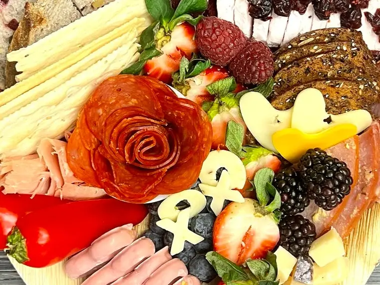 A heart-shaped charcuterie board full of a variety of meats, cheeses, fruits, and nuts sits on a table.