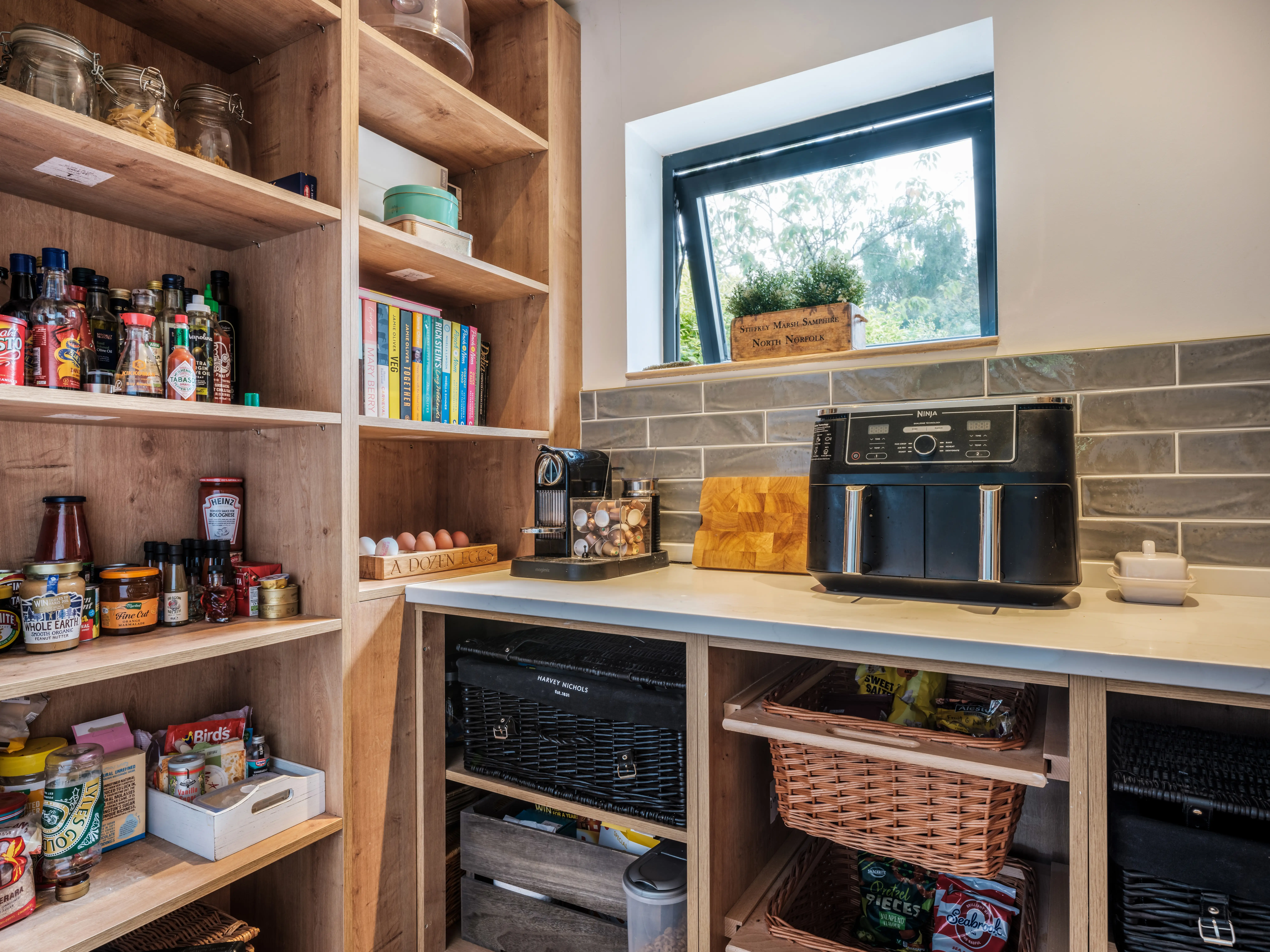 Open kitchen pantry shelves display condiments, cookbooks, eggs, baskets, a coffee machine and a black NINJA air fryer.