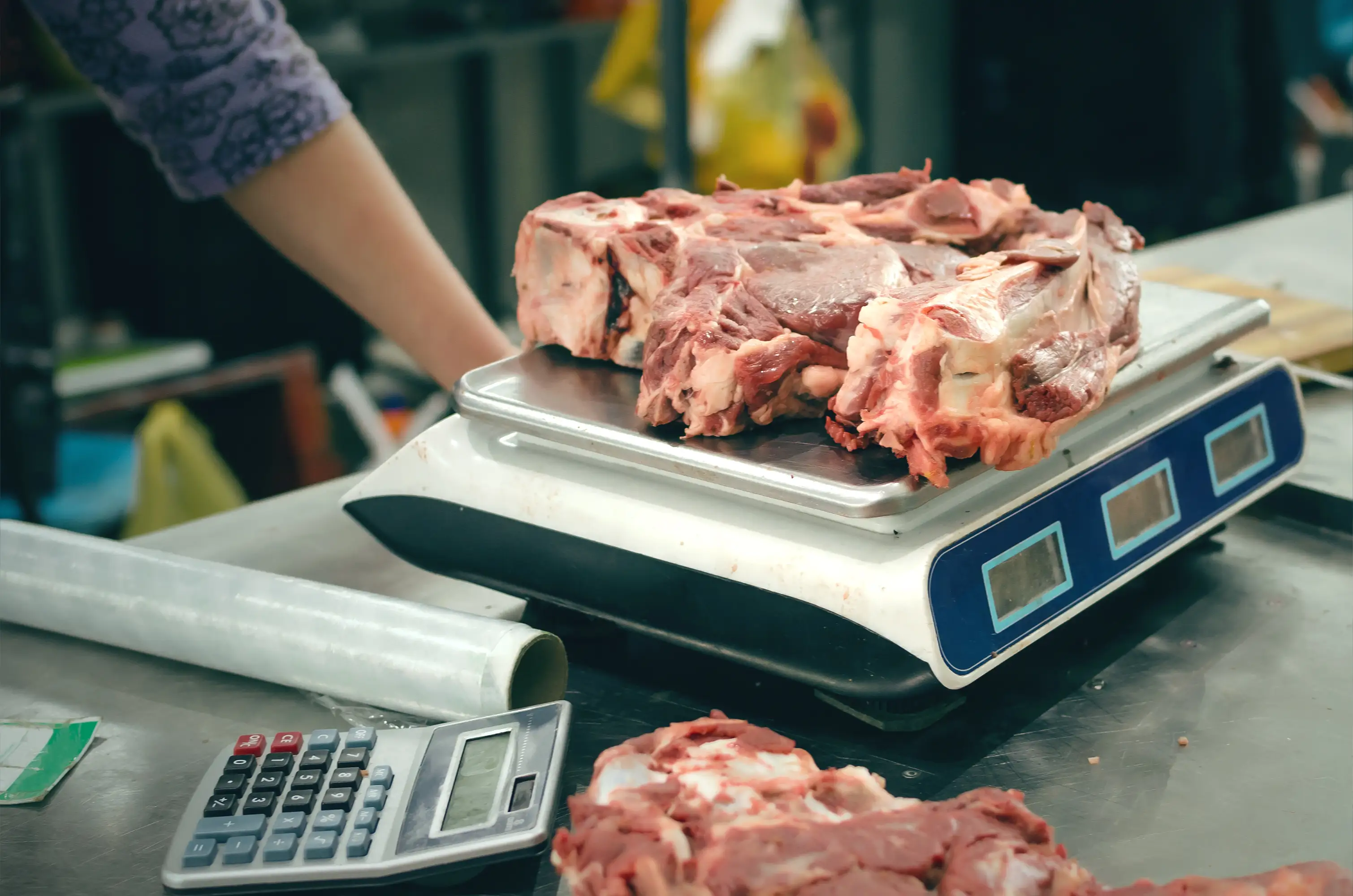 Raw meat is weighed on a digital scale beside a calculator at a market counter.