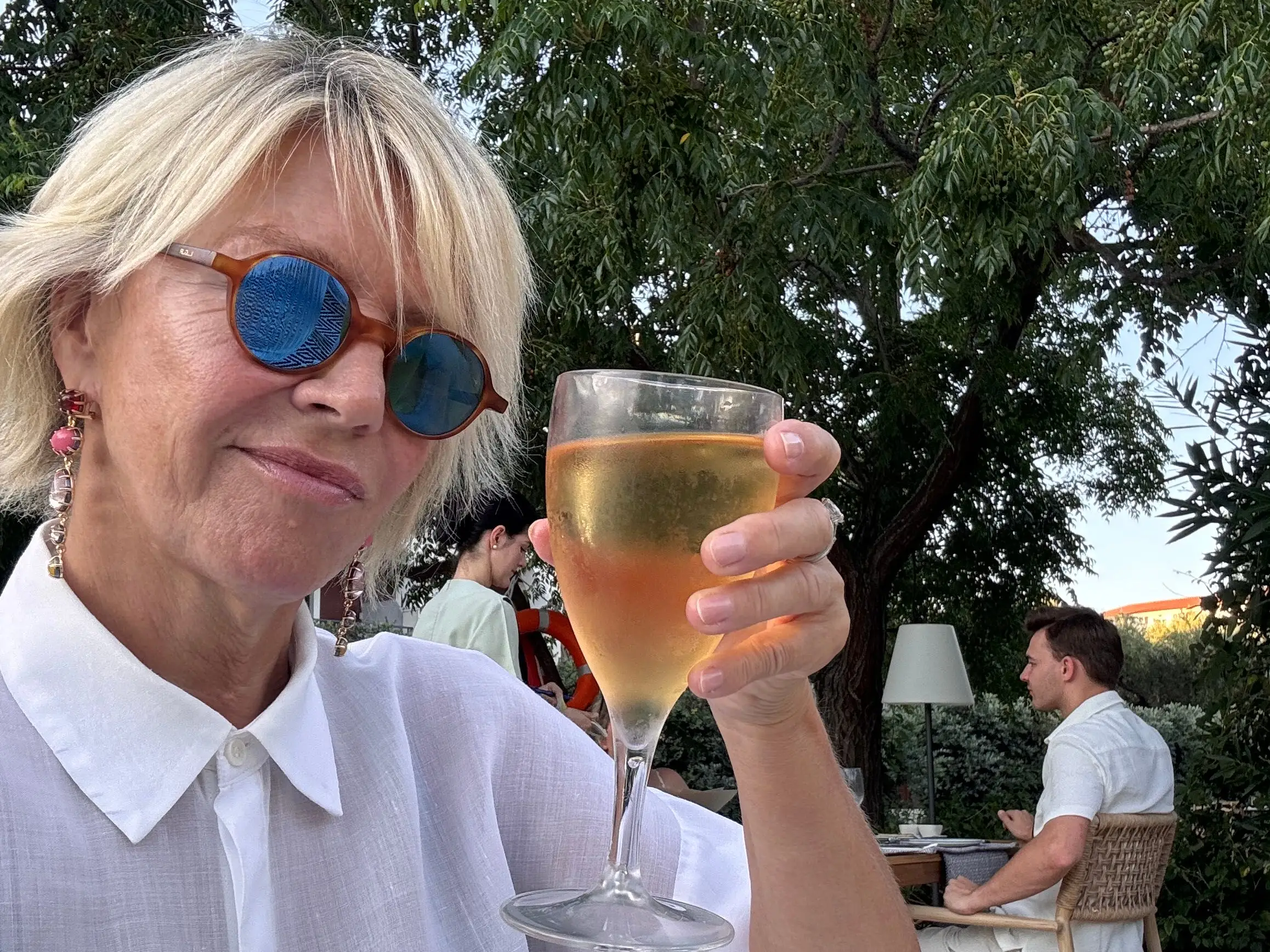 A woman in a white shirt holding up a glass of white wine.