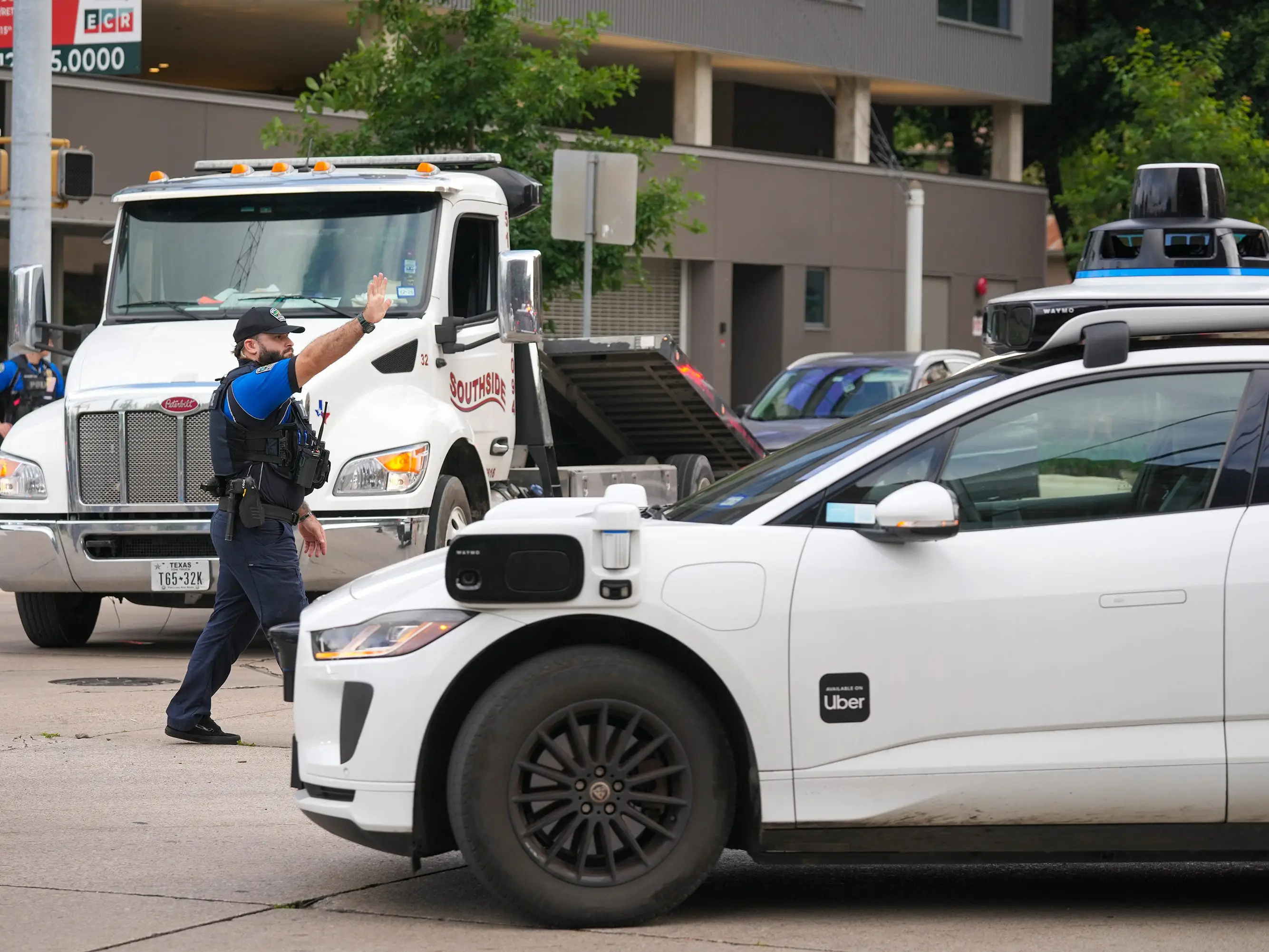 A police officer stands in the middle of a street where a Waymo robotaxi is driving by.