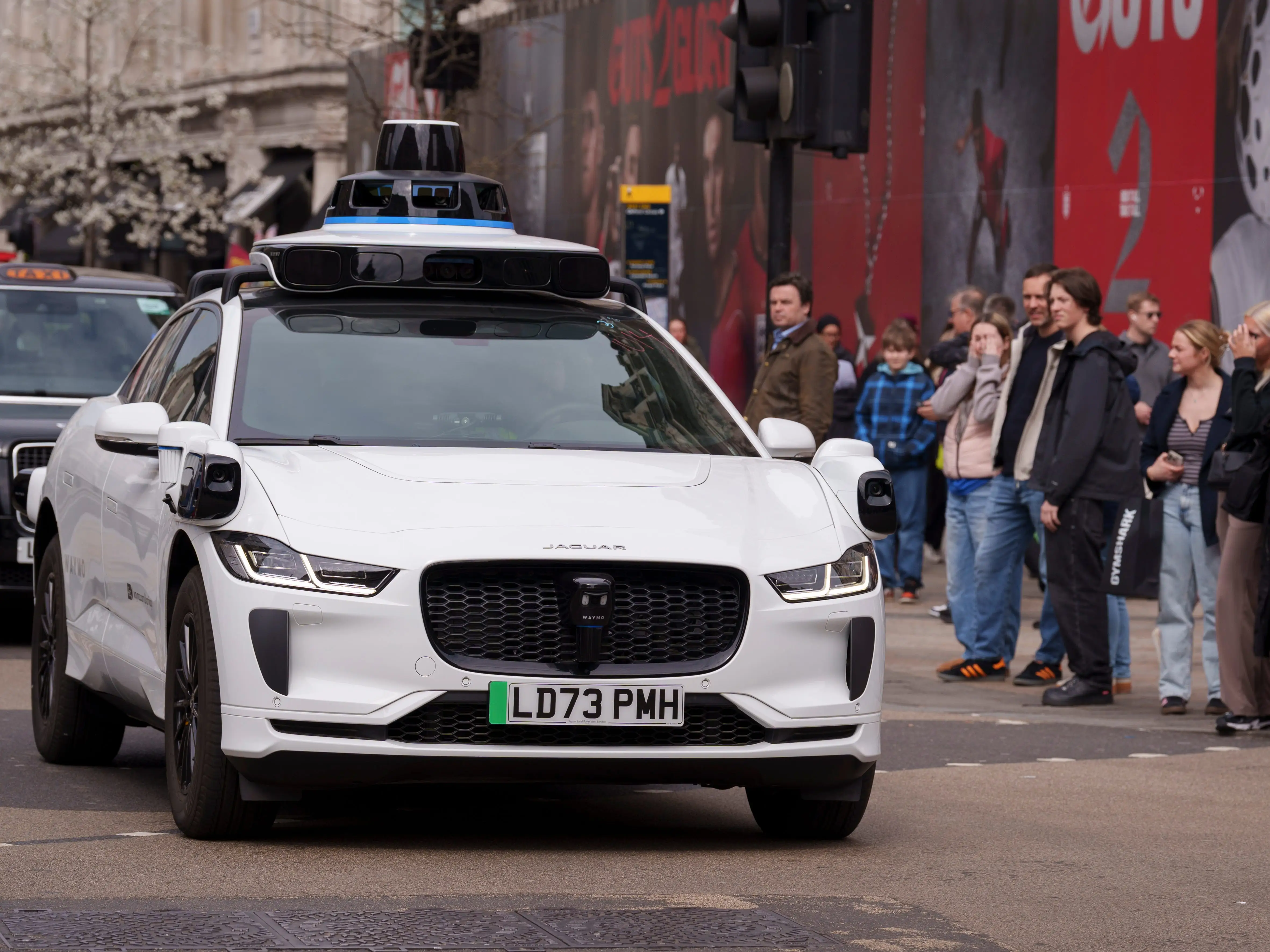 A Waymo robotaxi drives by a group of pedestrians.