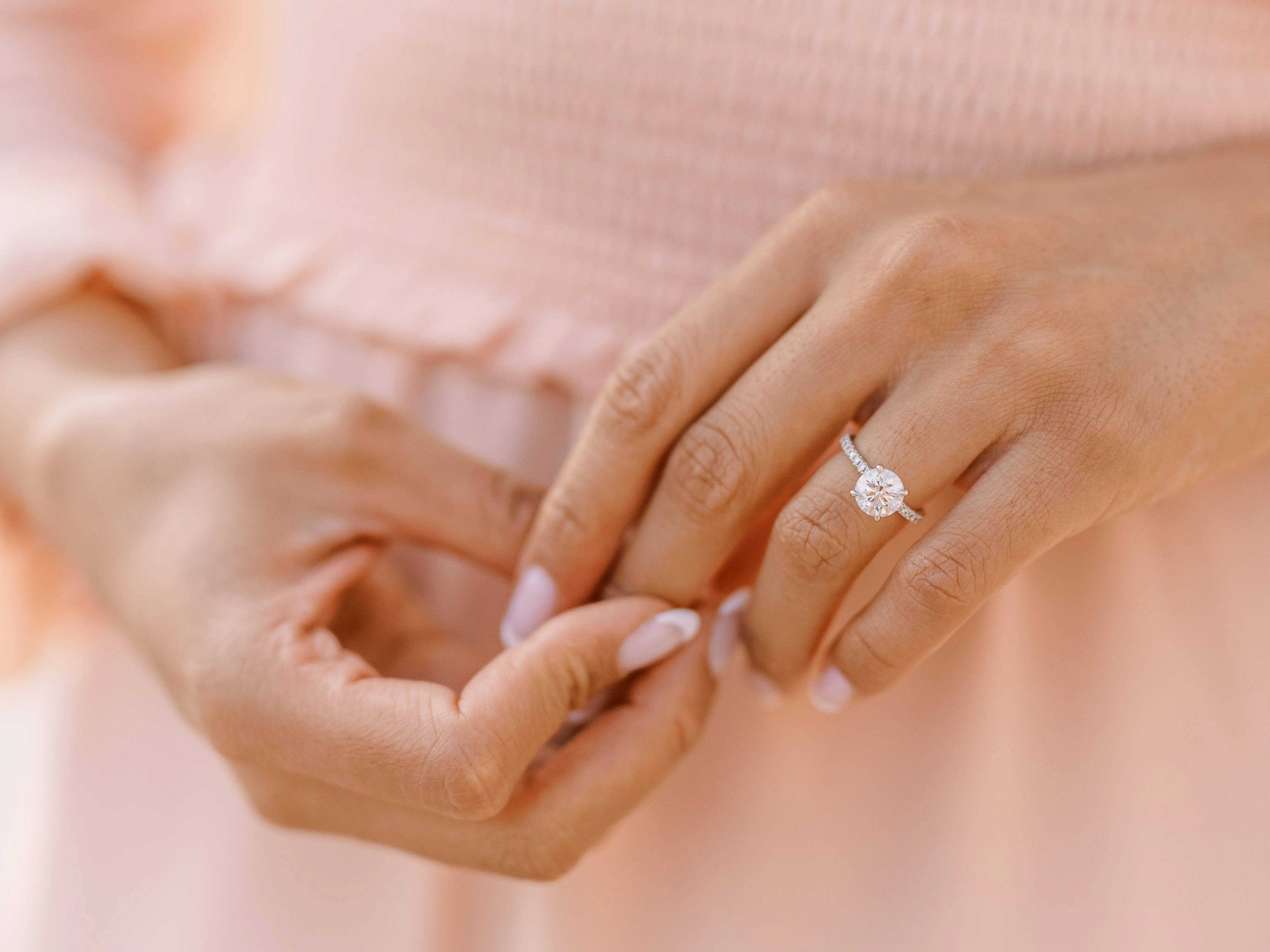 Close-up of hands adjusting a ring with a prominent gemstone against soft pink fabric.