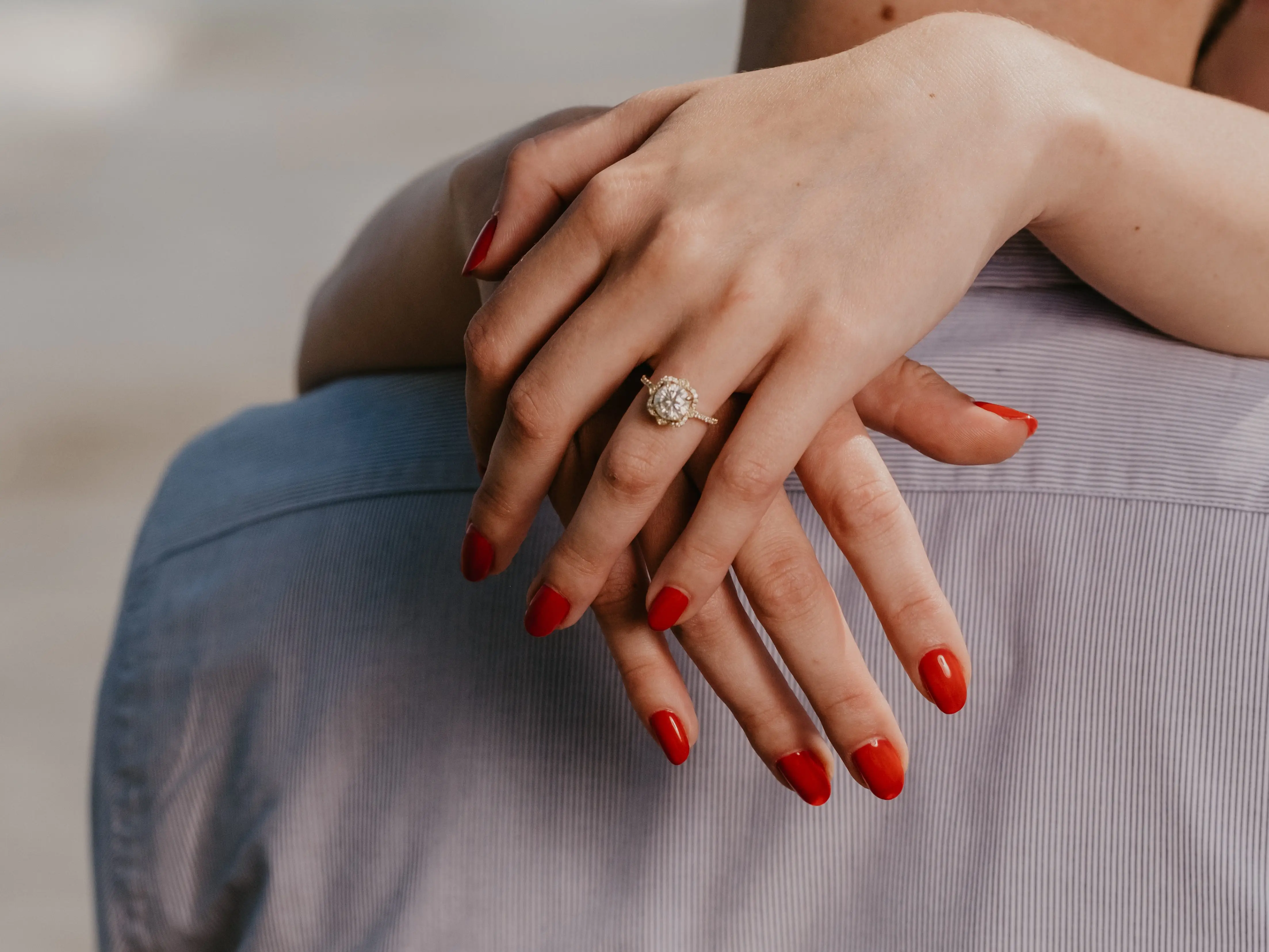 Hands with red nail polish and a diamond-style ring rest on a person's shoulder in a close-up embrace.