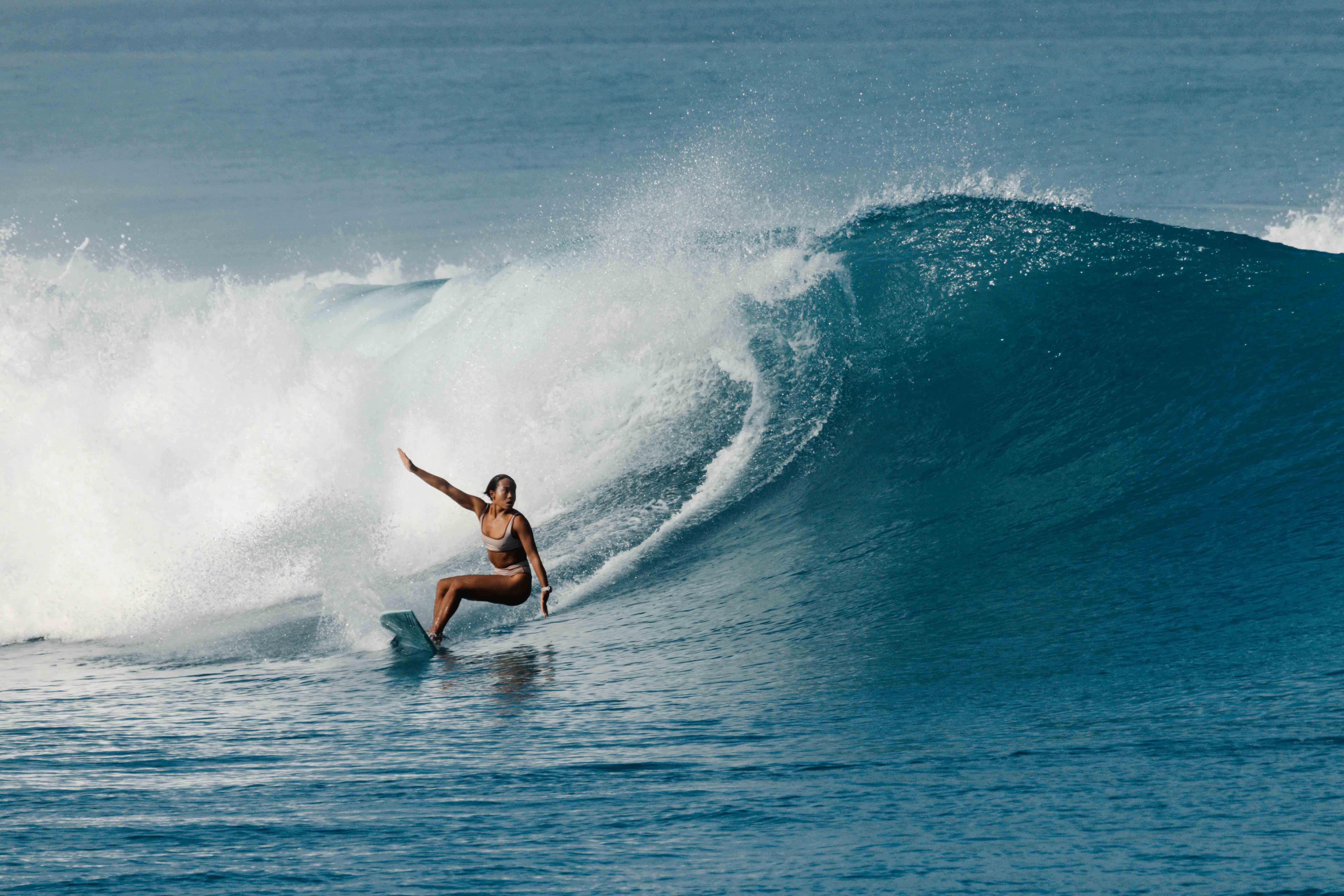 Alice Kim surfing with waves in the background as she rides the waves with one hand stretched to the sky.