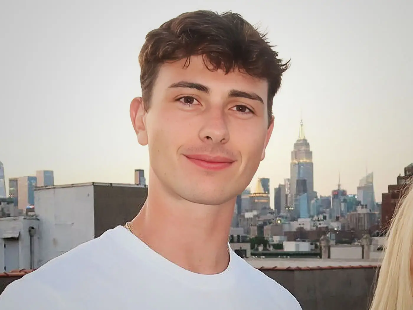 A young man smiles at a camera; the Empire State Building is in the background.