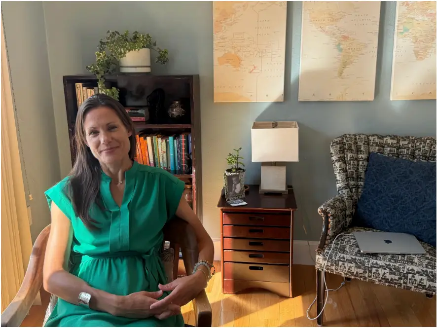 A woman in a green dress sitting in an armchair with a map in the background.