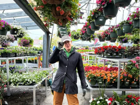 A woman at a garden center alongside hanging and potted plants.