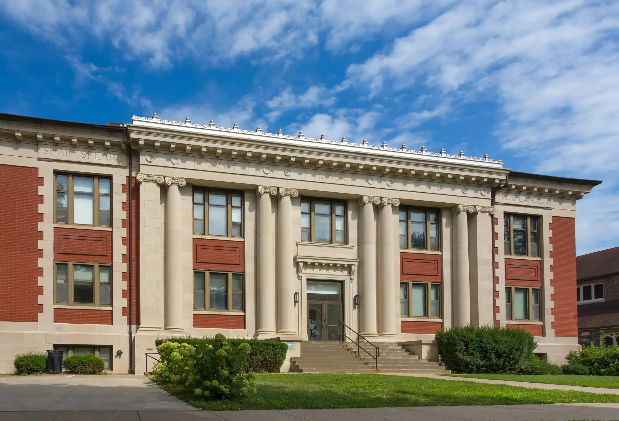 Classical brick and stone facade of Carnegie Hall on the campus of Grinnell College under a blue sky with clouds.