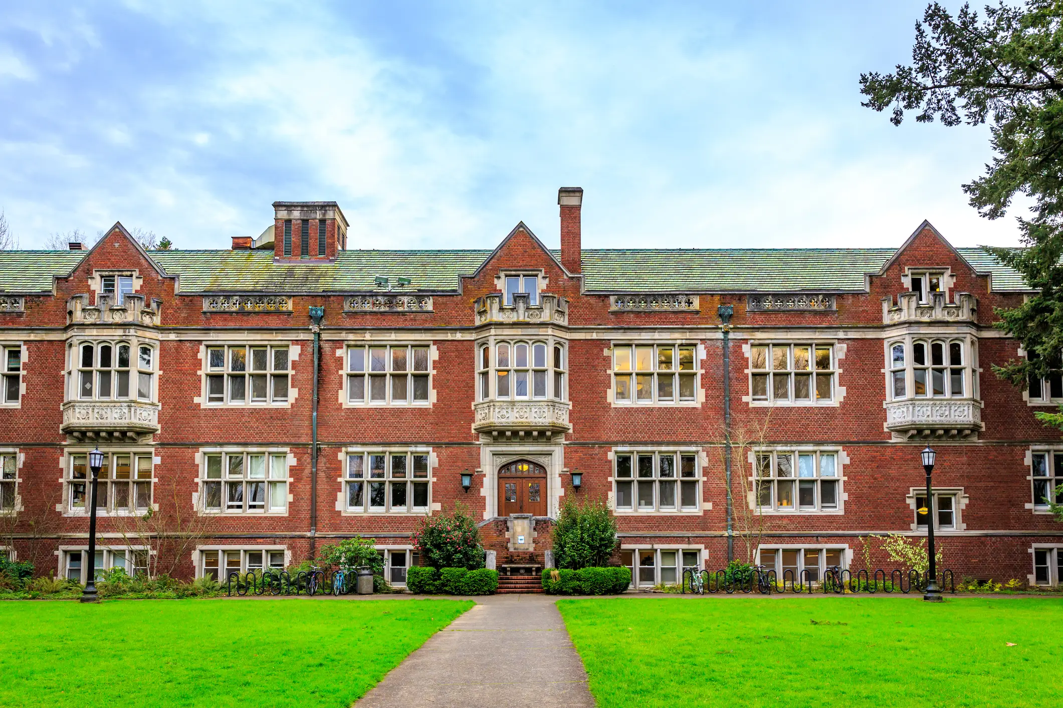 Reed College's red-brick institutional building, with bay windows and a central entrance, faces a green lawn and walkway.