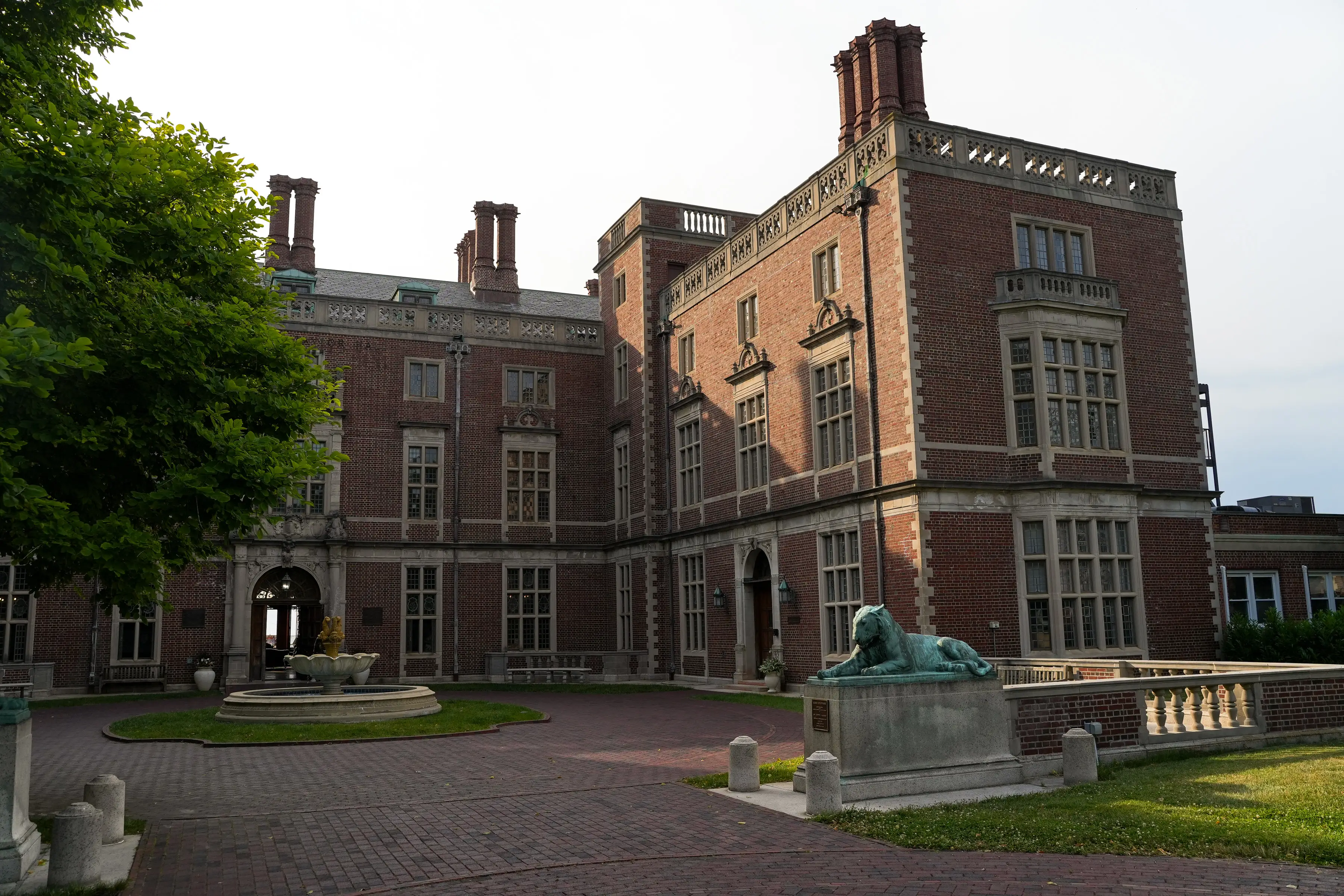 Webb Institute building with tall chimneys, arched entry, courtyard fountain, and reclining statue on a pedestal.