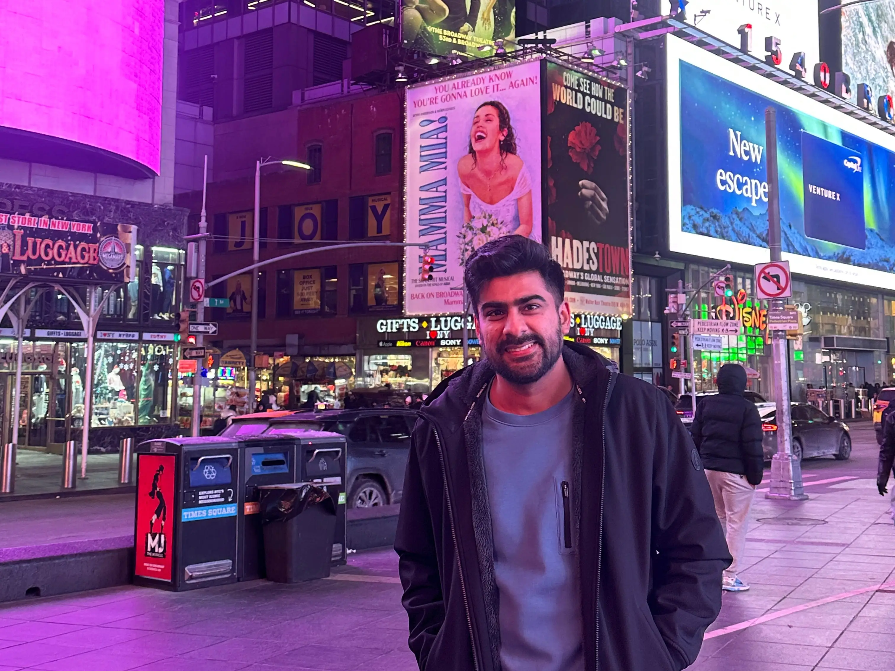 Madhur Mehta is smiling in front of some billboards at night.