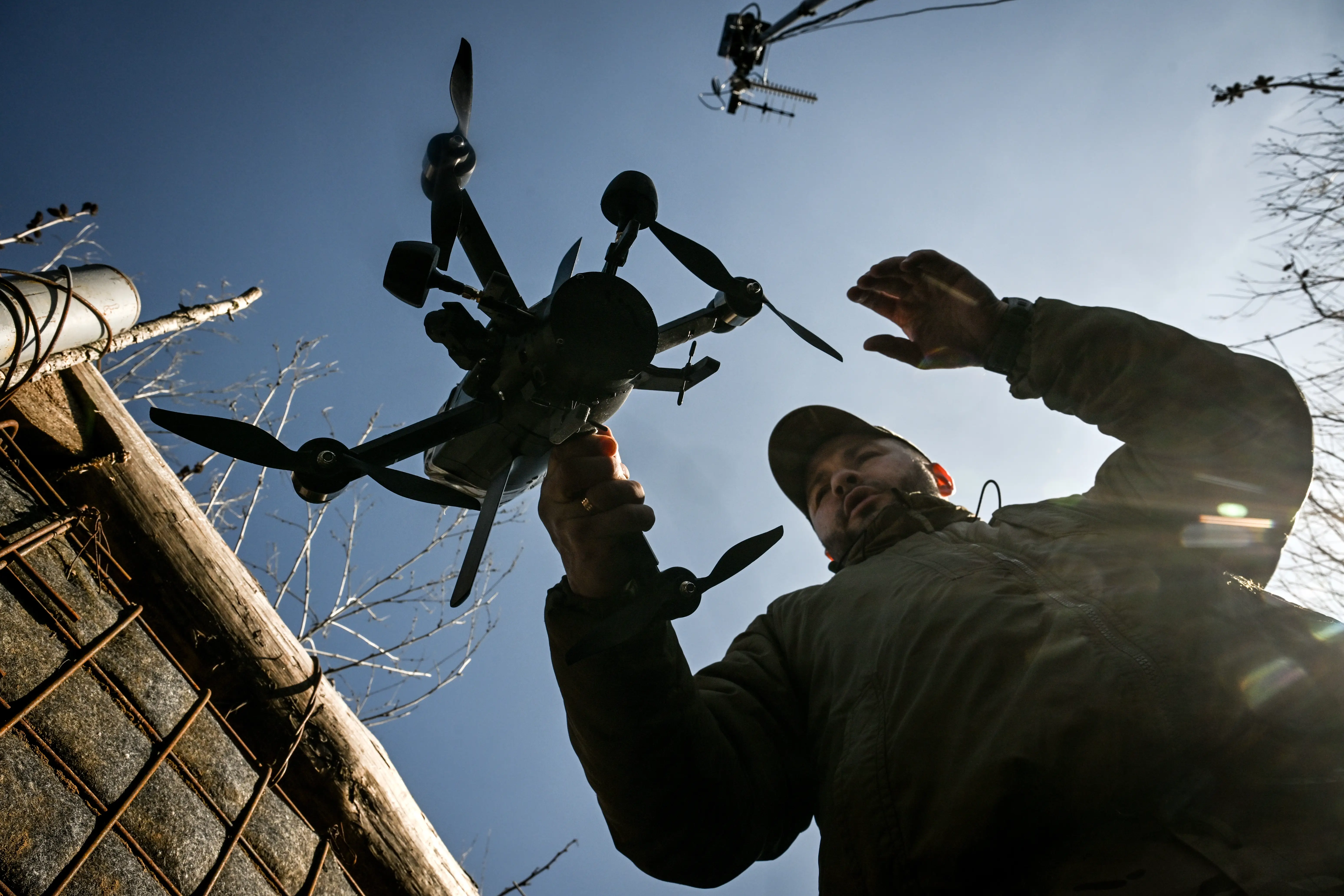 A person holds a multi-rotor drone beside a utility pole under a bright blue sky.