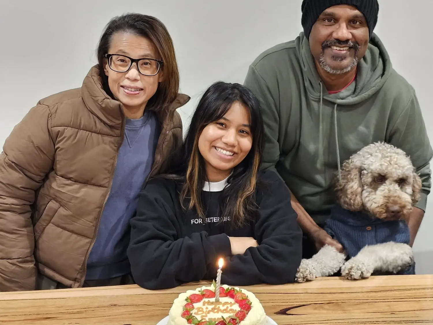 The writer sitting in between her parents, with a birthday cake in front of her and a curly-haired dog nearby.