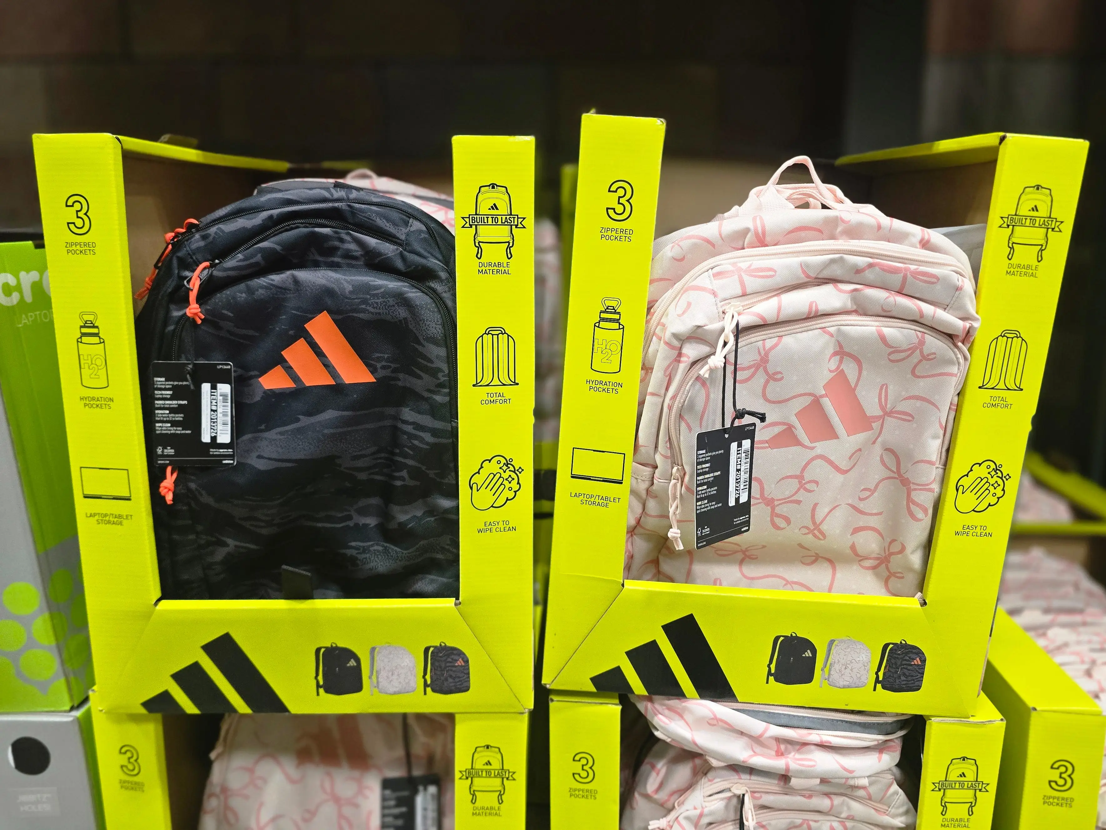 Two Adidas backpacks — one black and one pink — in boxes at Costco.