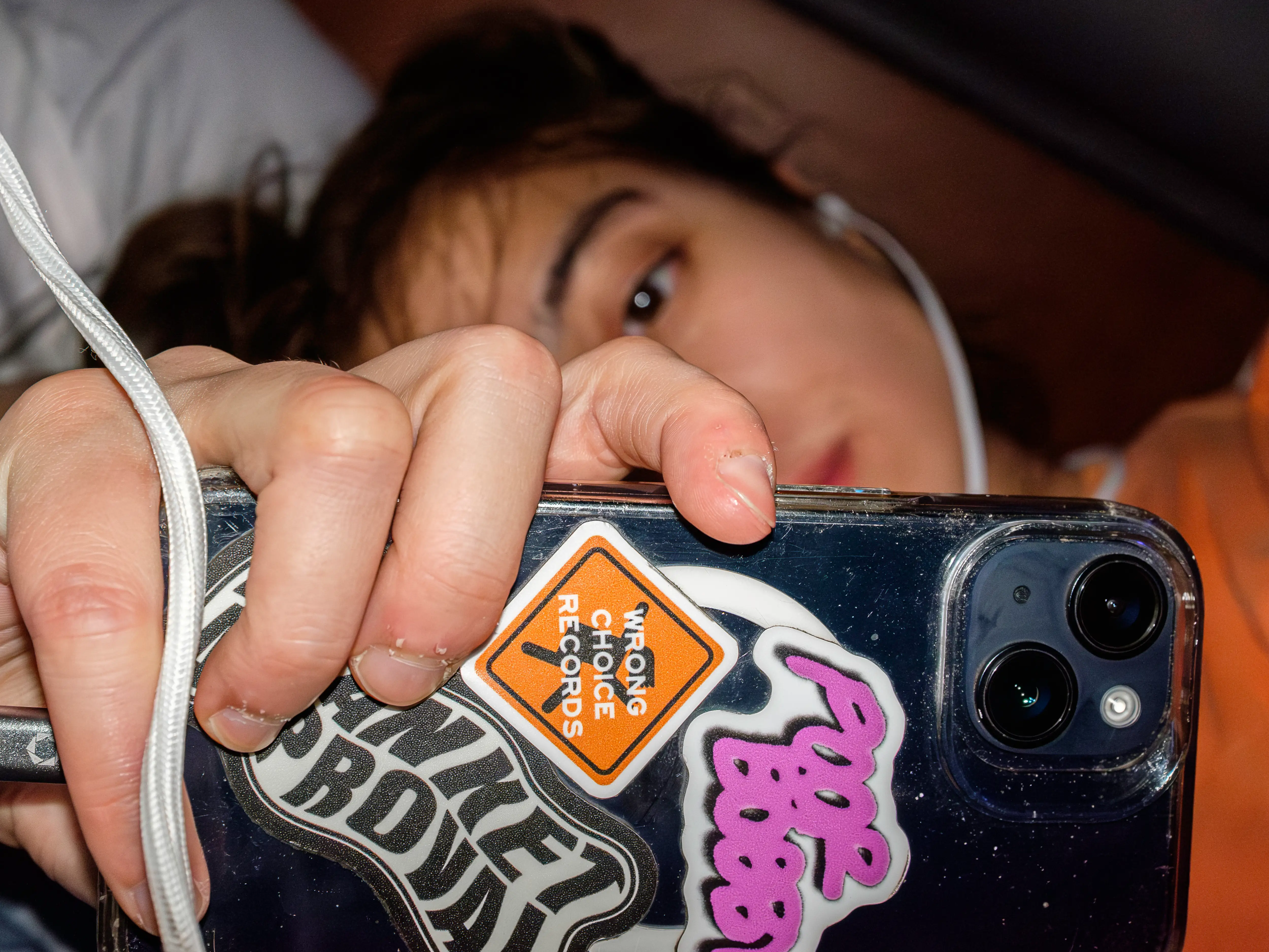 Close-up of a person lying down while holding a sticker-covered smartphone near their face.